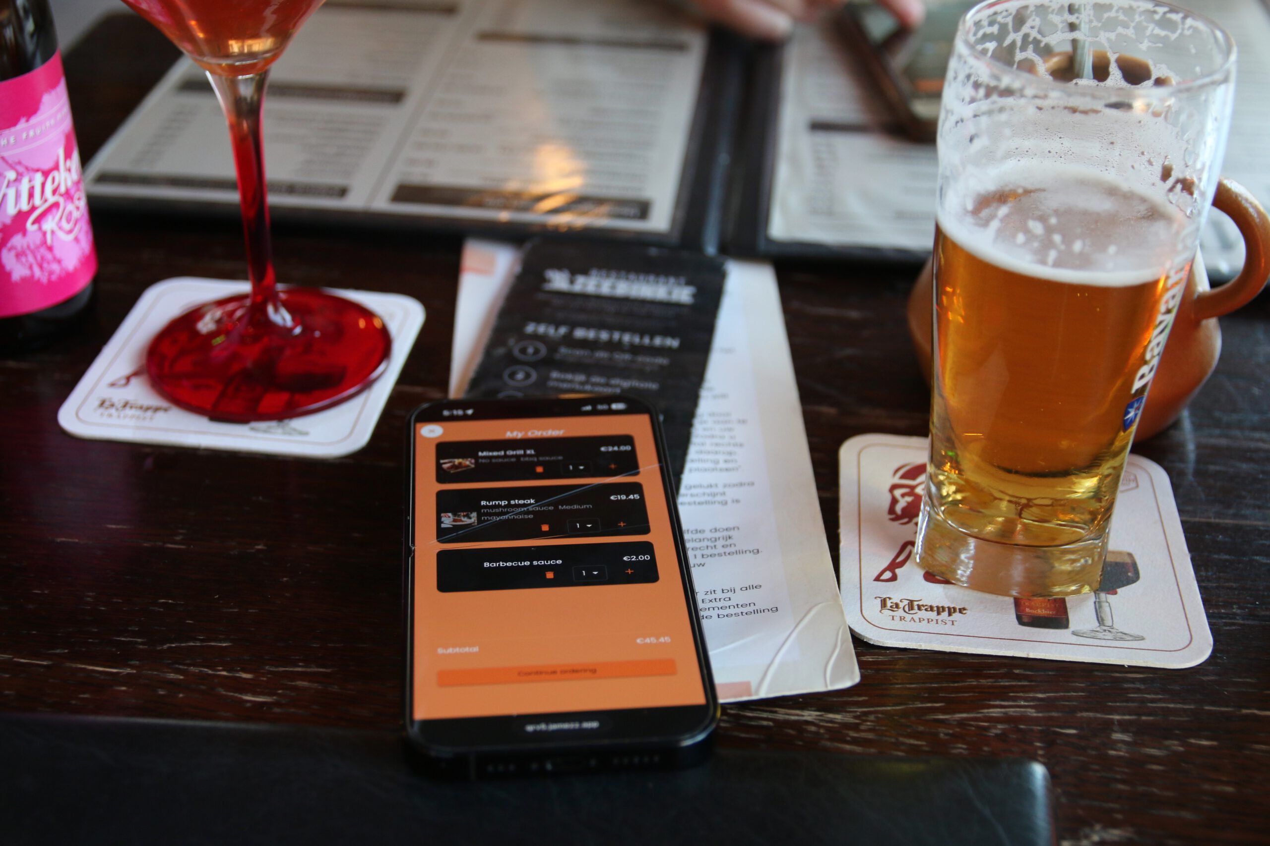 Restaurant Zeebinkie review, smartphone with QR ordering system open on table inside Restaurant Zeebinkie in Burgh Haamstede showing Mixed Grill XL and rump steak order next to Bavaria Pilsener lager and Wittekerke Rosé beer