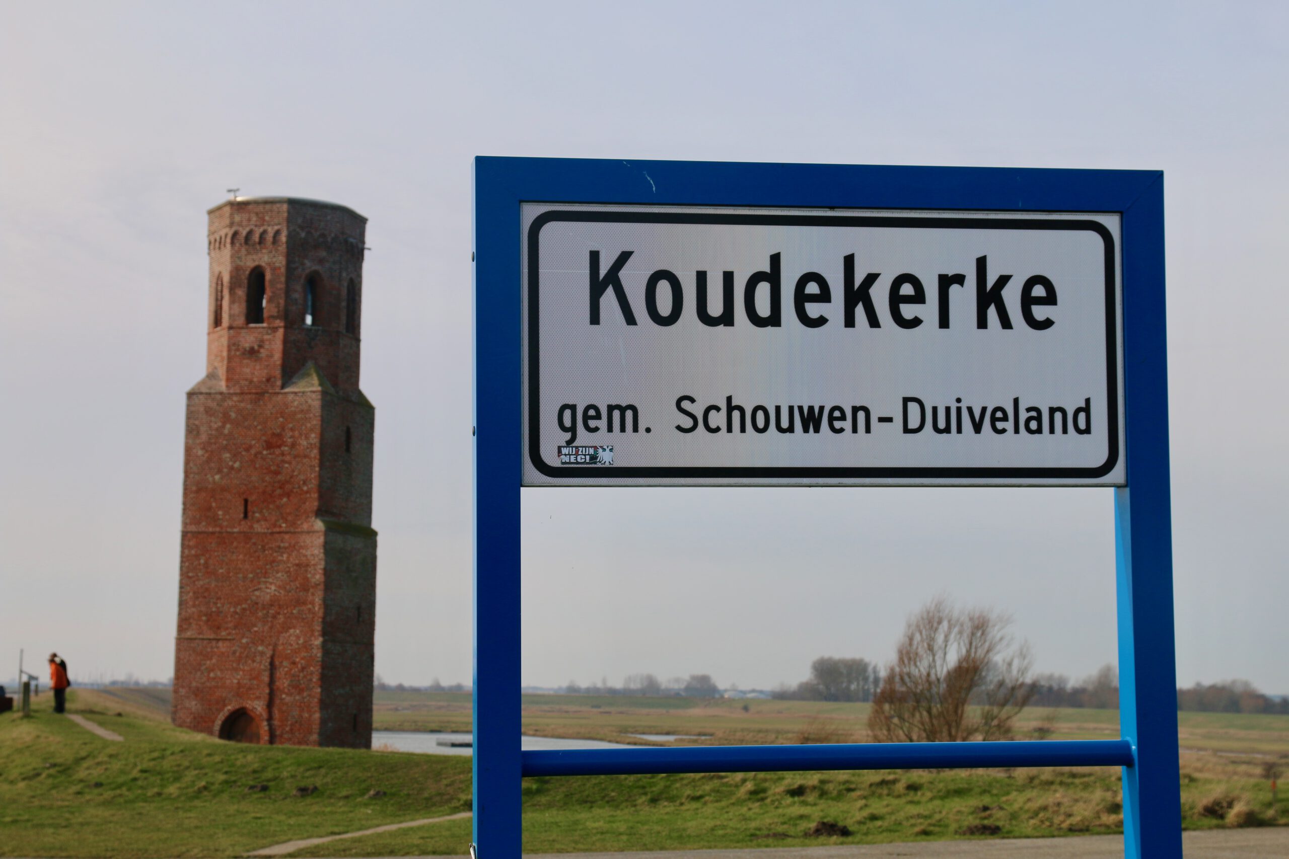 Plompe Toren Koudekerke behind the Koudekerke village sign in Schouwen Duiveland, Zeeland landscape with historic brick tower in the background