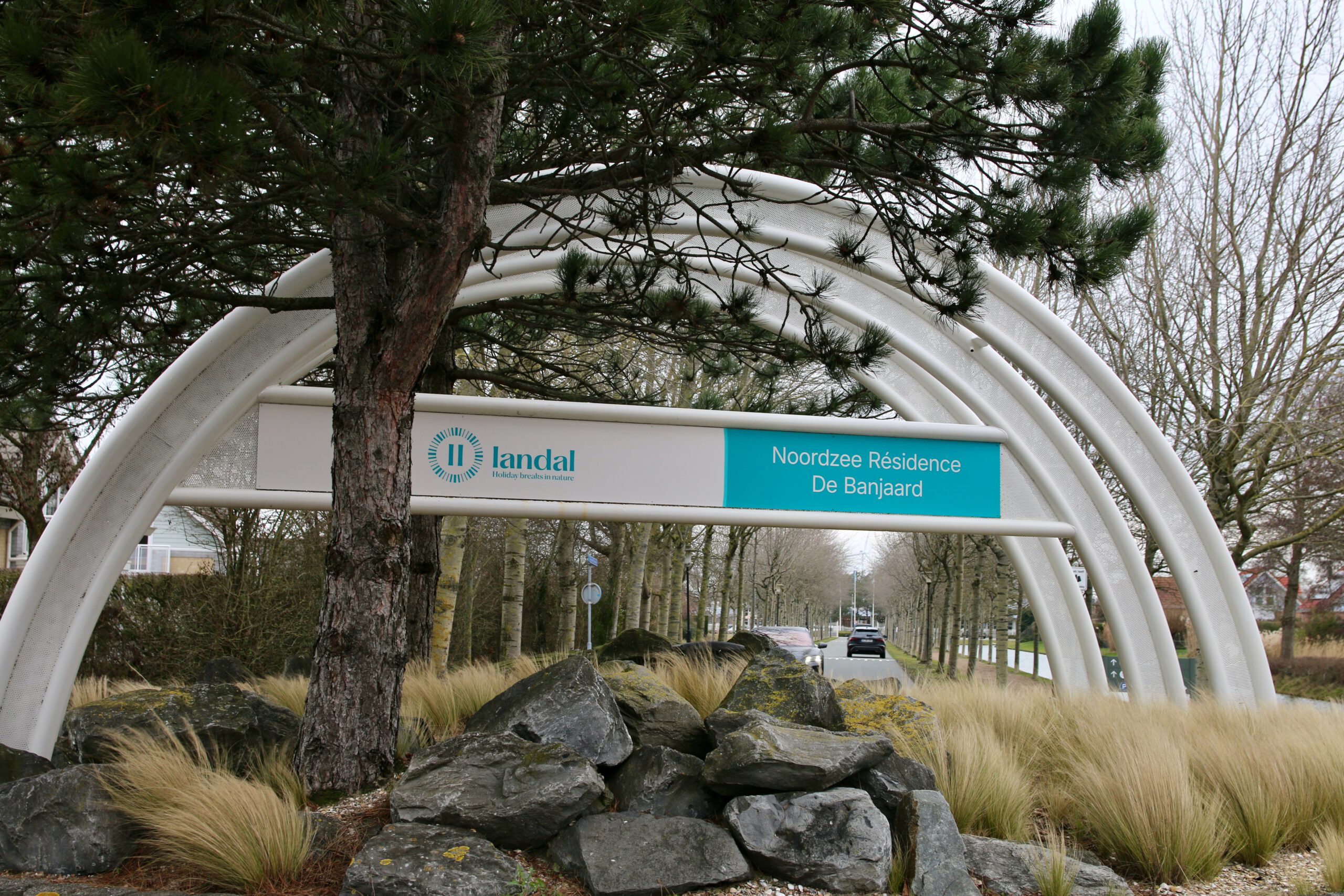 Landal Noordzee Résidence De Banjaard entrance sign in Kamperland, Zeeland, modern white arch structure with Landal logo surrounded by dune grass and natural stone landscaping