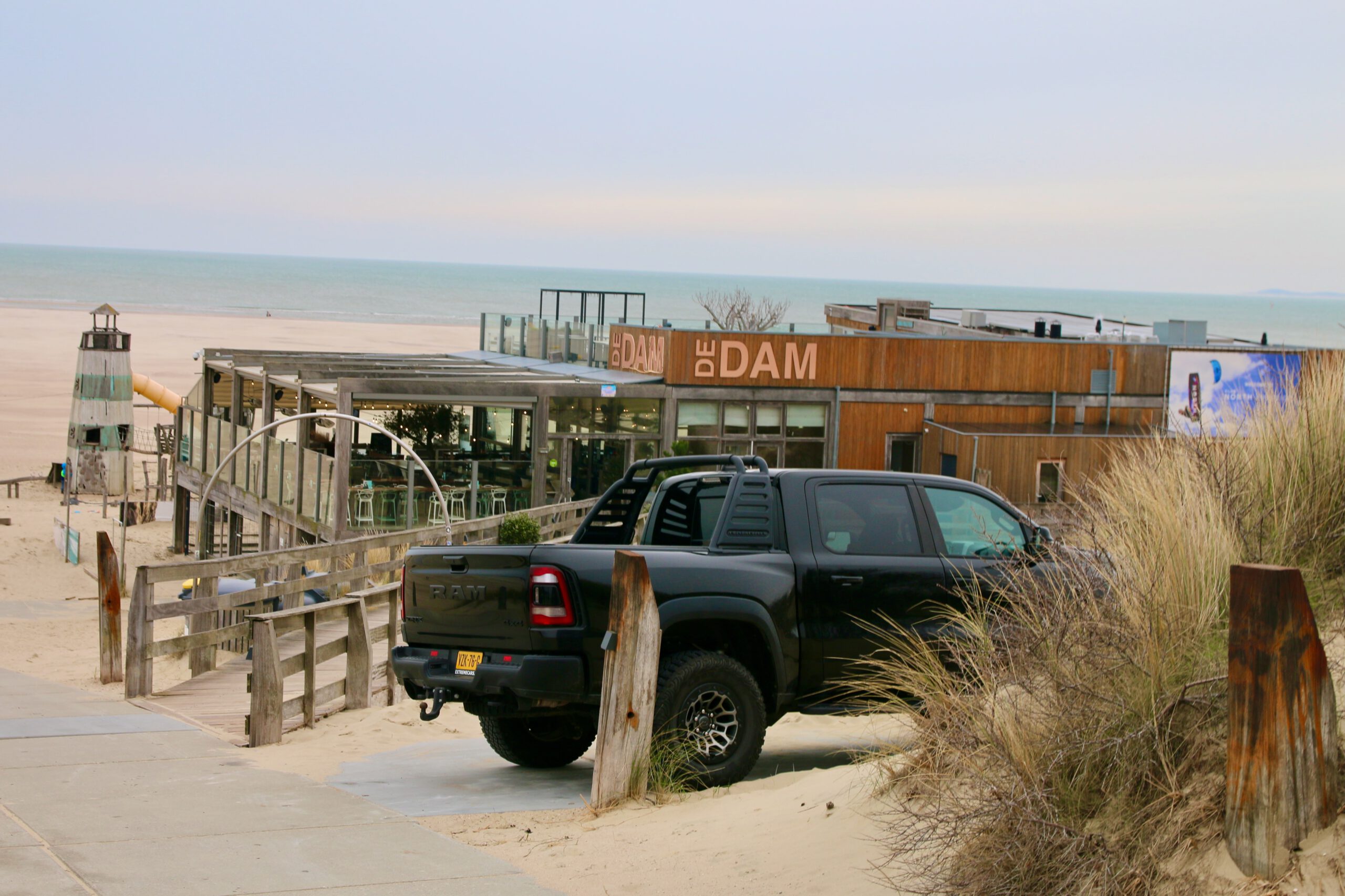 Strandrestaurant De Dam review view of the beach pavilion at Strand 80 Vrouwenpolder with wooden exterior, rooftop terrace and black RAM pickup truck parked in the dunes near the North Sea.