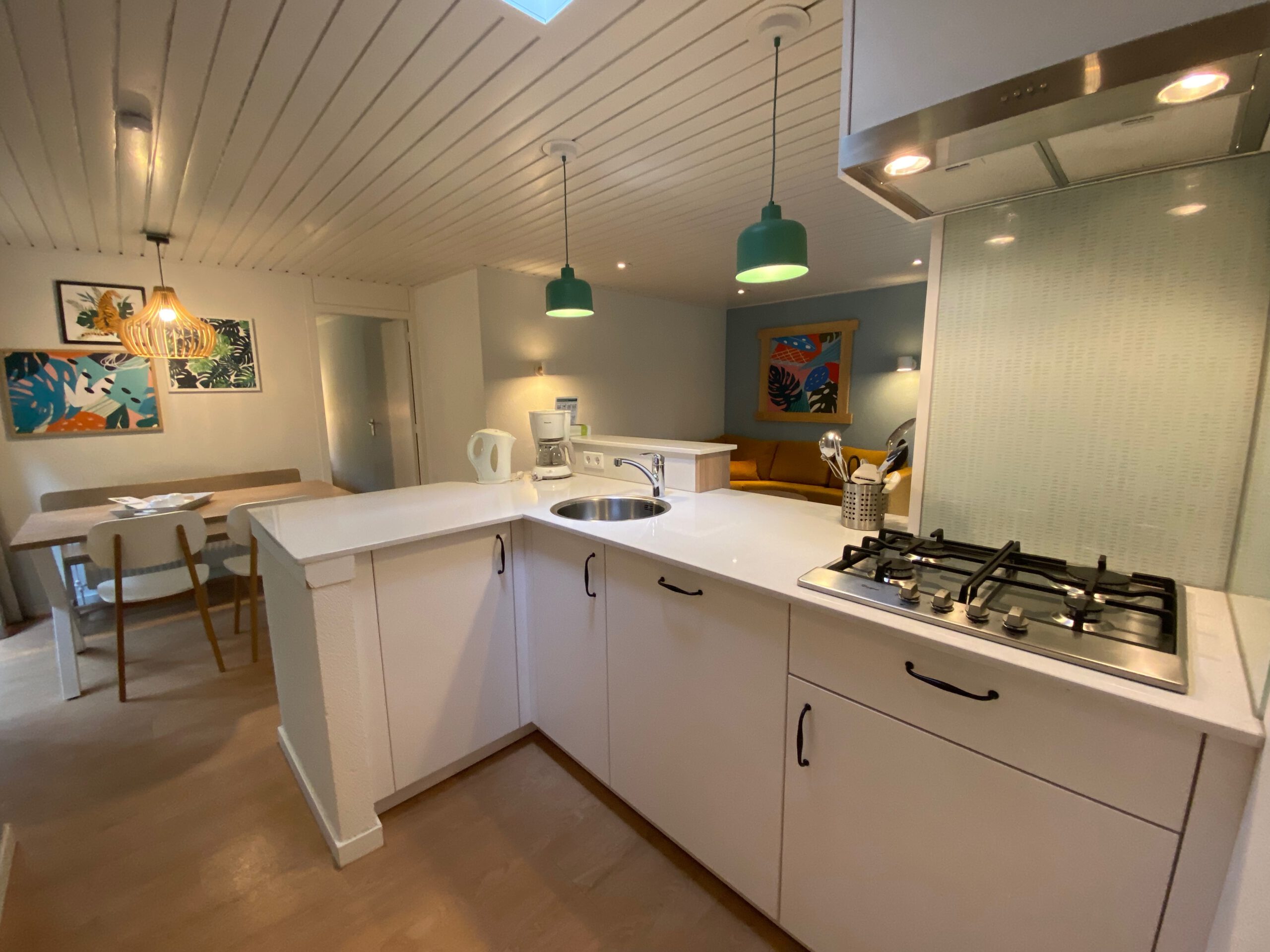 Modern kitchen and dining area inside Center Parcs Het Heijderbos 4 pers. Premium HB1922 cottage 965, featuring gas stove, white cabinetry, dining table, green pendant lights and open living layout.