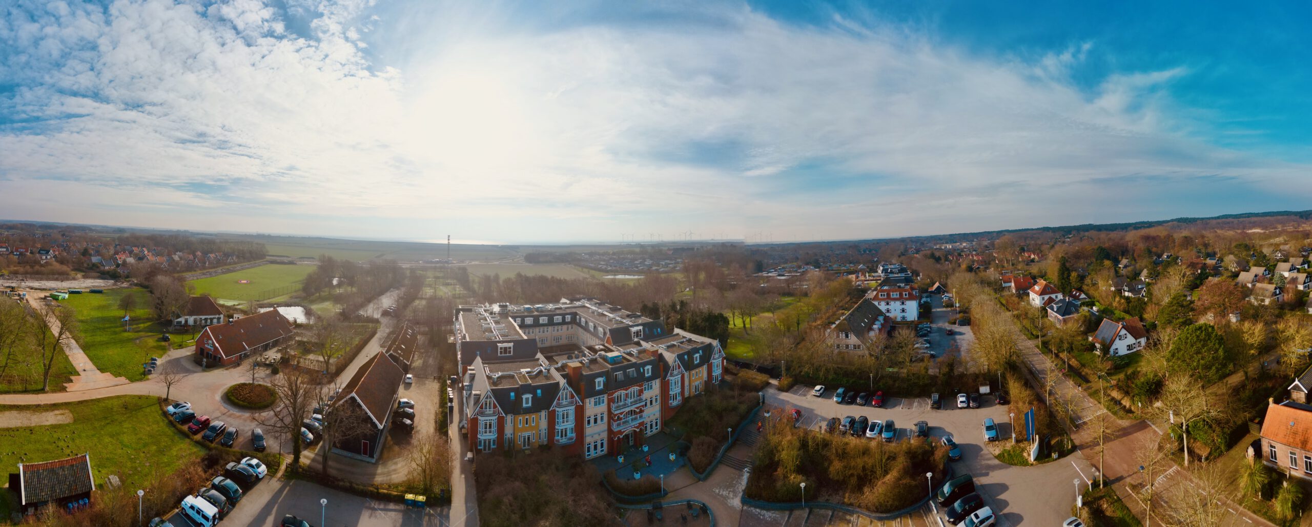 Grand Hotel Ter Duin review panoramic drone view showing the hotel in Burgh Haamstede surrounded by countryside, residential houses, parking areas, and open Zeeland landscape under a wide blue sky