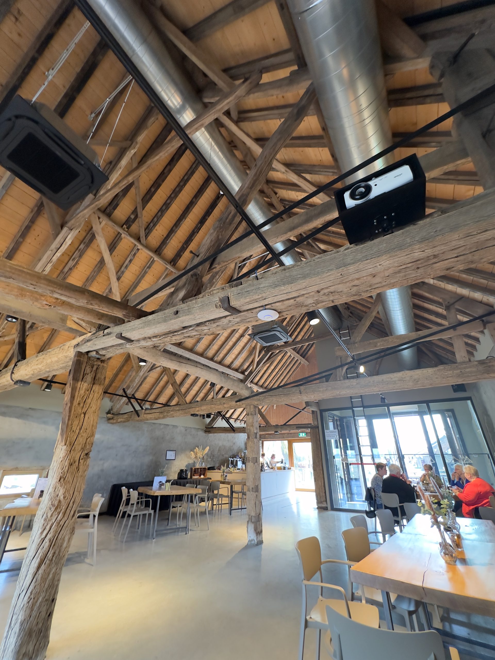 De Hompesche Molen interior in Stevensweert, with high wooden beams, a spacious dining area, rustic architecture, and a modern café setting in Limburg