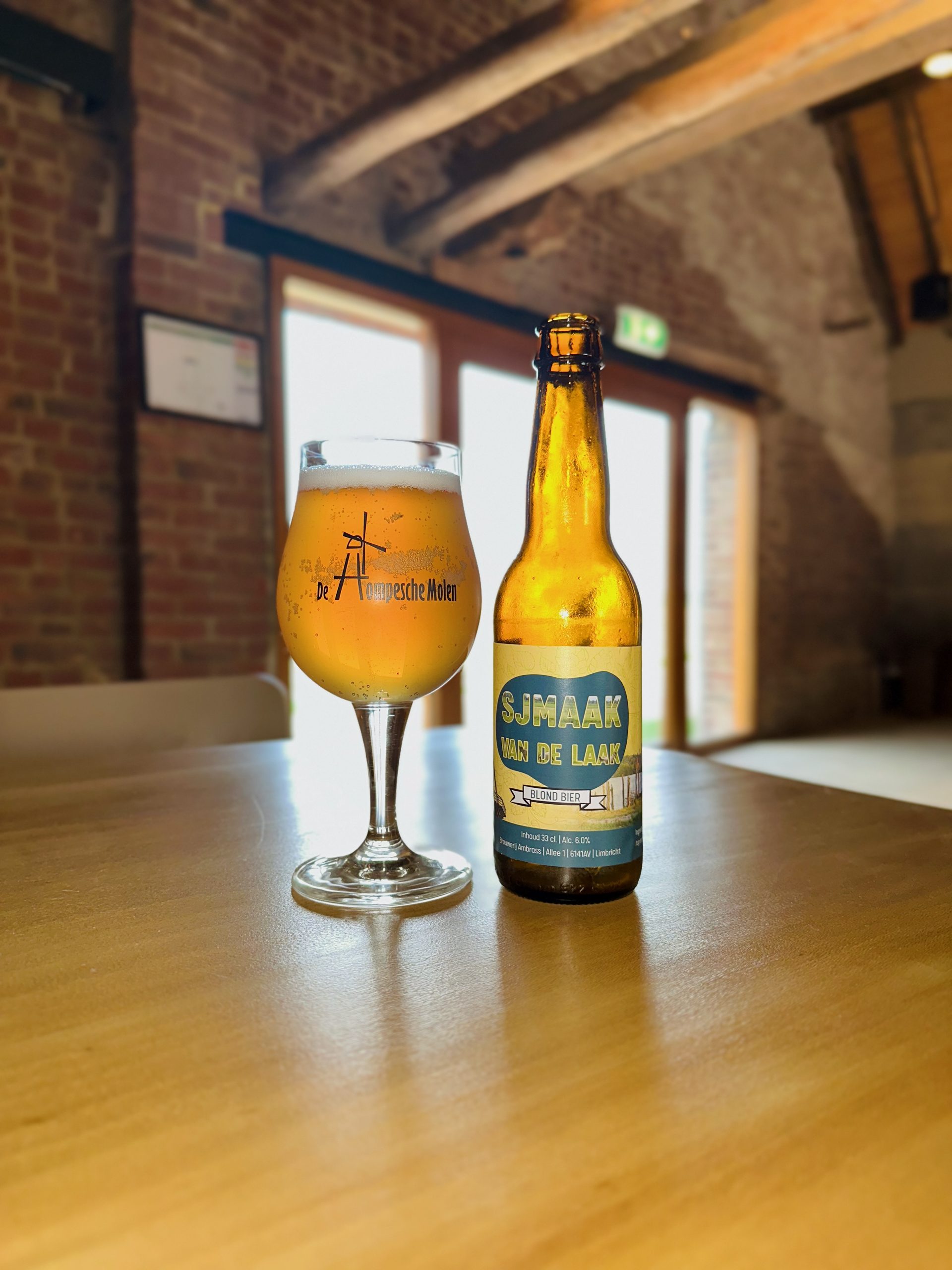 De Hompesche Molen local beer Sjmaak van de Laak served indoors at the historic mill in Stevensweert, with a branded glass, warm light, and rustic brick interior