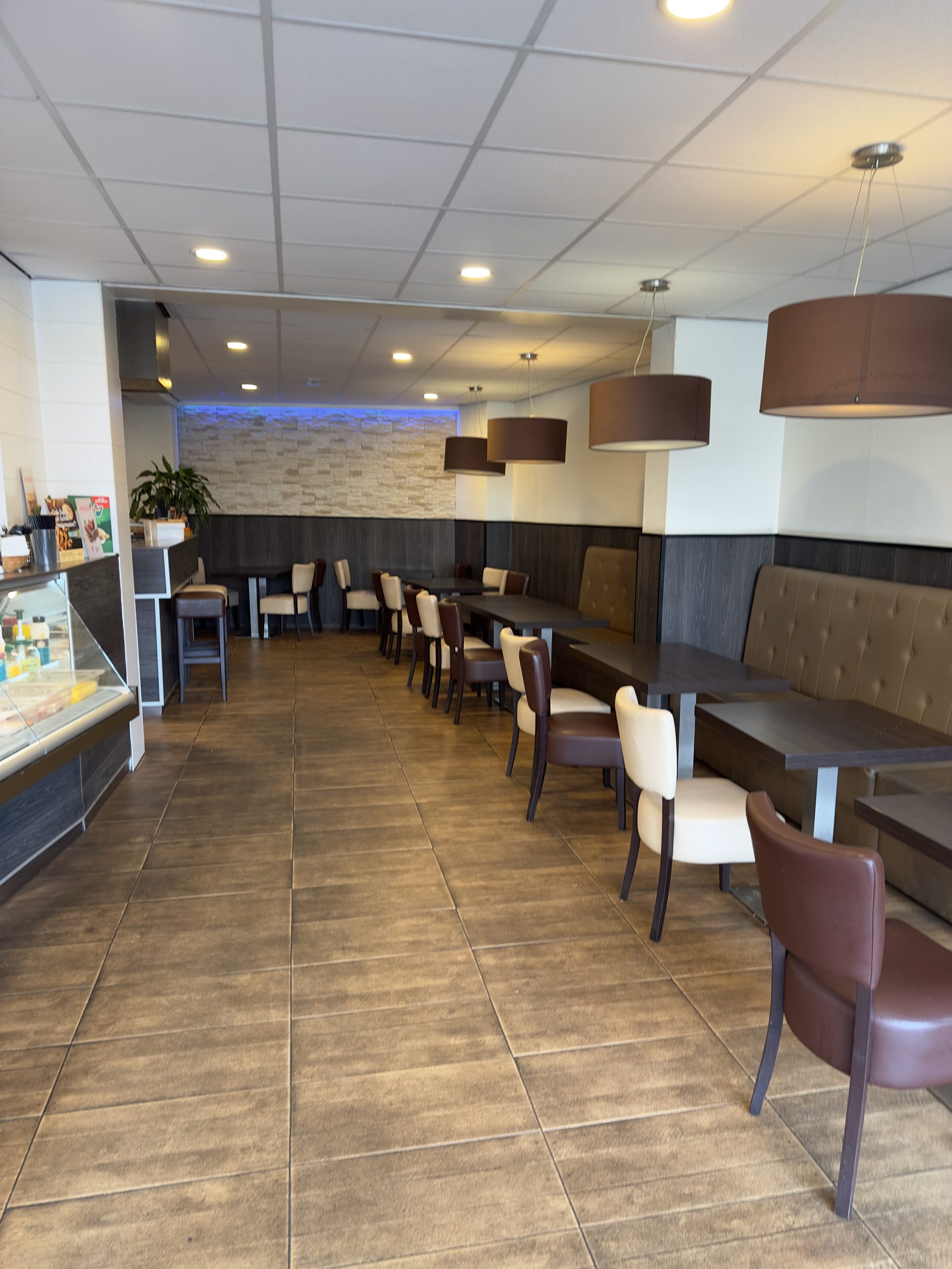 Cafetaria De Molen Maasbracht interior with spacious seating area, brown chairs, booth seating, pendant lights, and modern snack bar dining space