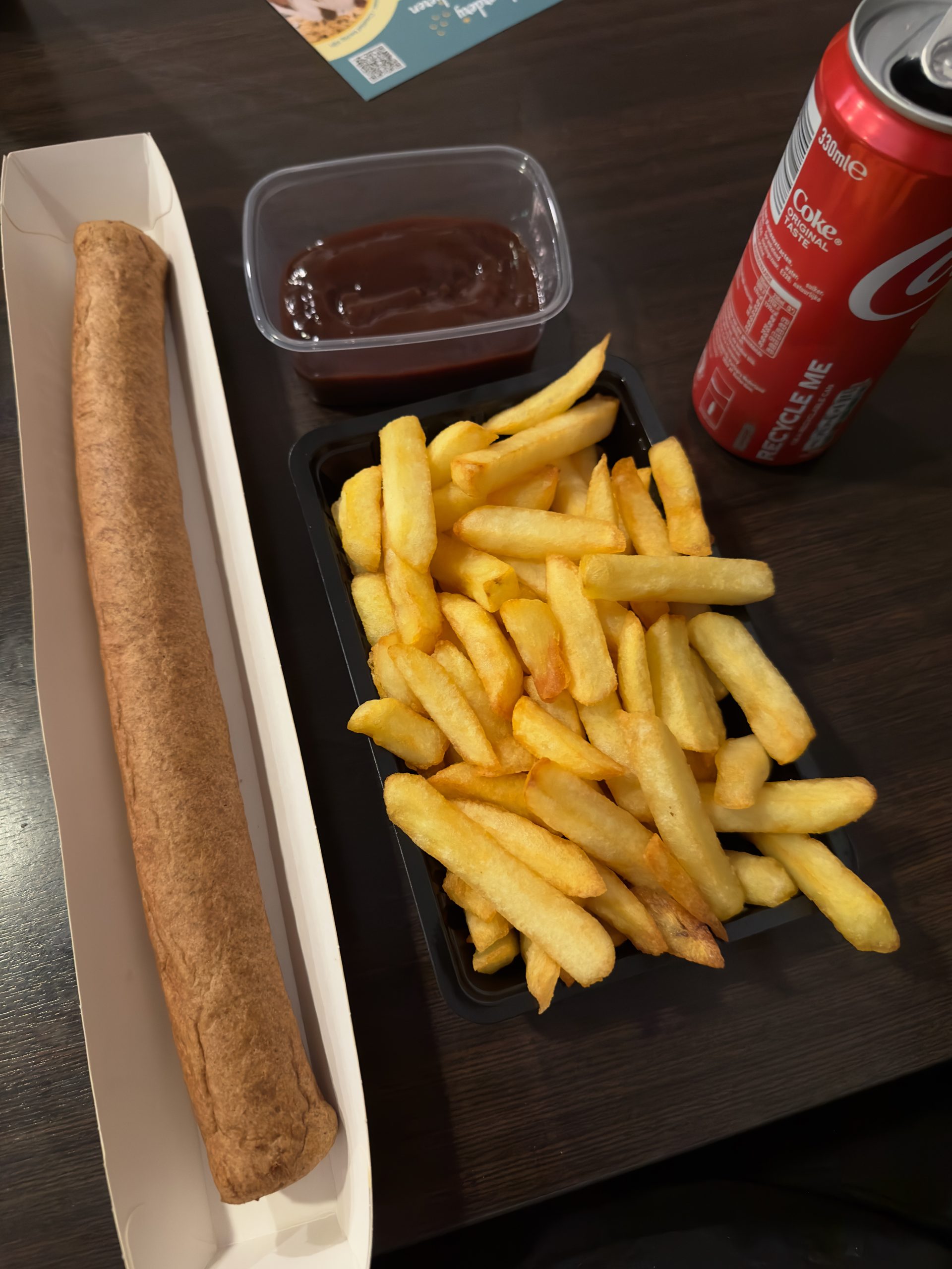 Cafetaria De Molen Maasbracht meal with medium fries, XXL frikandel, Coca Cola, and sauce served on a dark wooden table