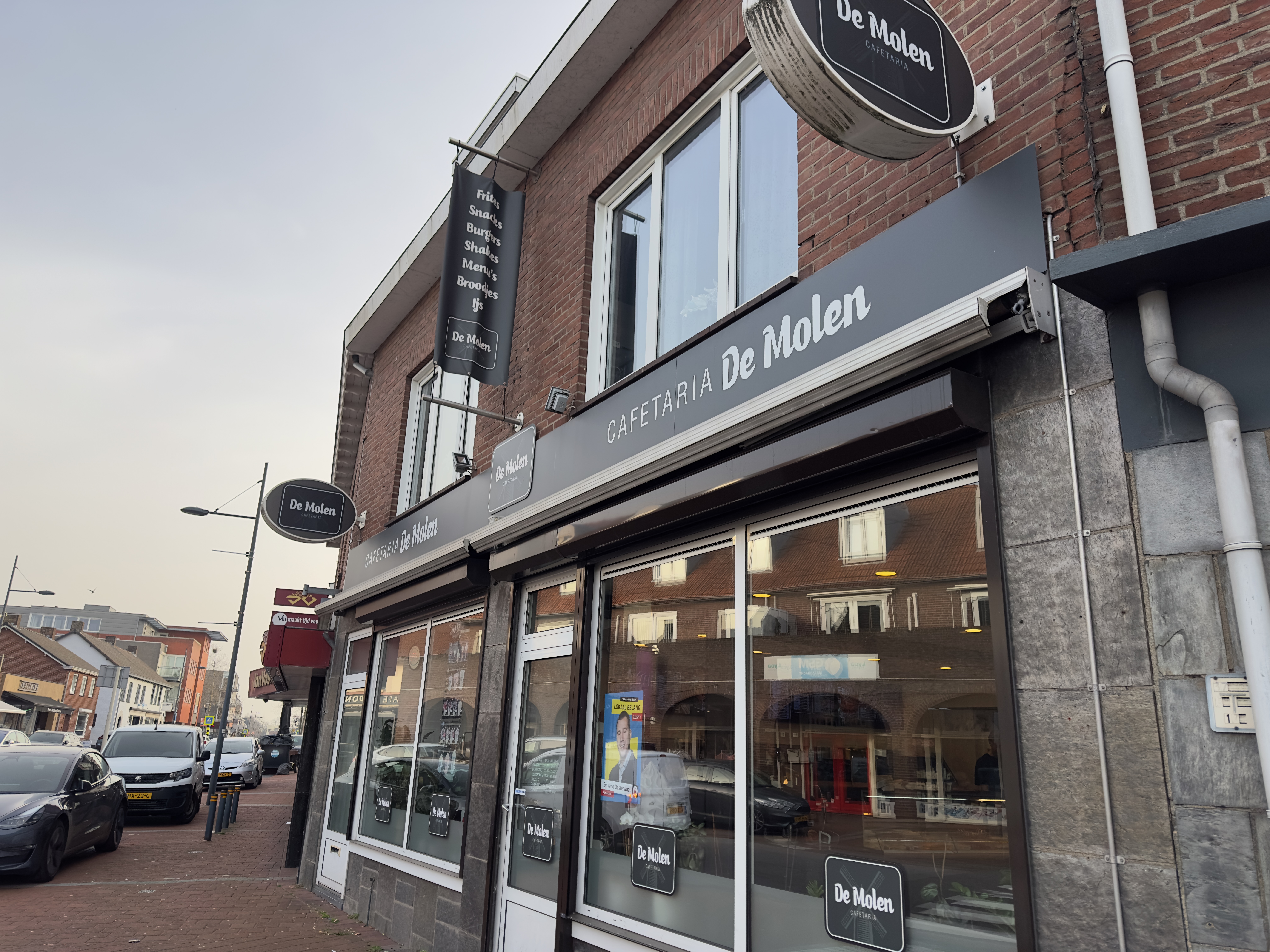 Cafetaria De Molen Maasbracht exterior storefront in Maasbracht with black signage, brick facade, and street view of the local cafetaria