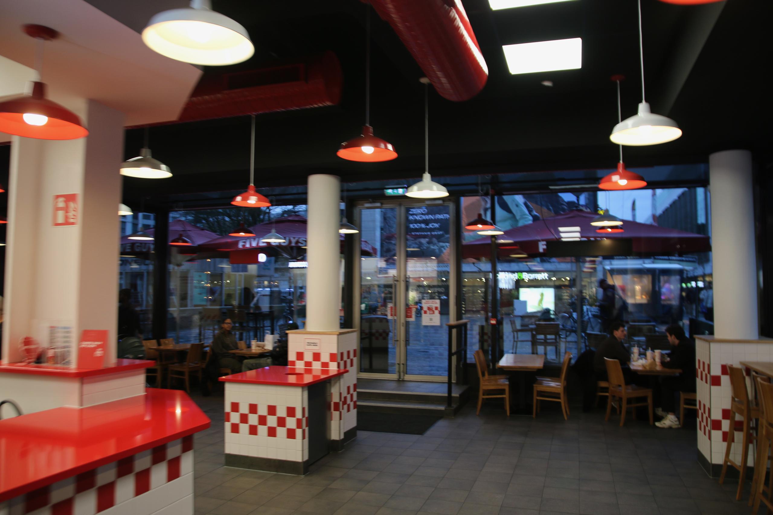 Atmosphere inside Five Guys Netherlands with red pendant lights, tiled counters and visible entrance to the city center terrace