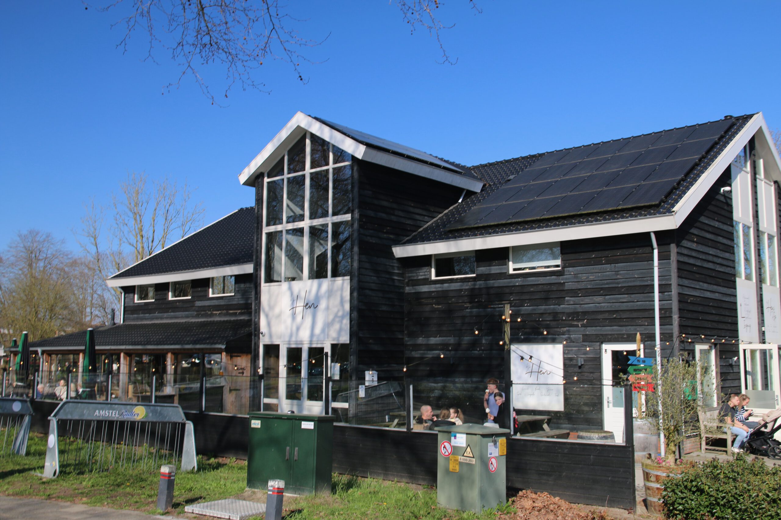 Bij Hen Alphen aan den Rijn exterior view of the black wooden restaurant building with sunny terrace in Park Zegersloot