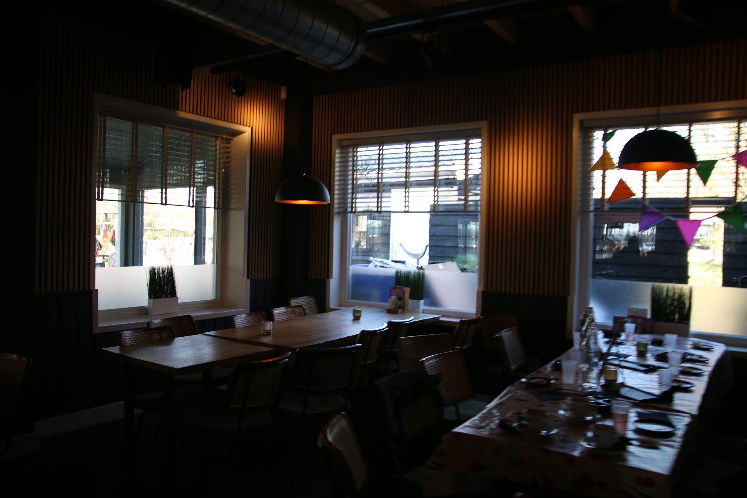 Bij Hen Alphen aan den Rijn cozy indoor seating area with large wooden tables, warm lighting, and a relaxed restaurant atmosphere