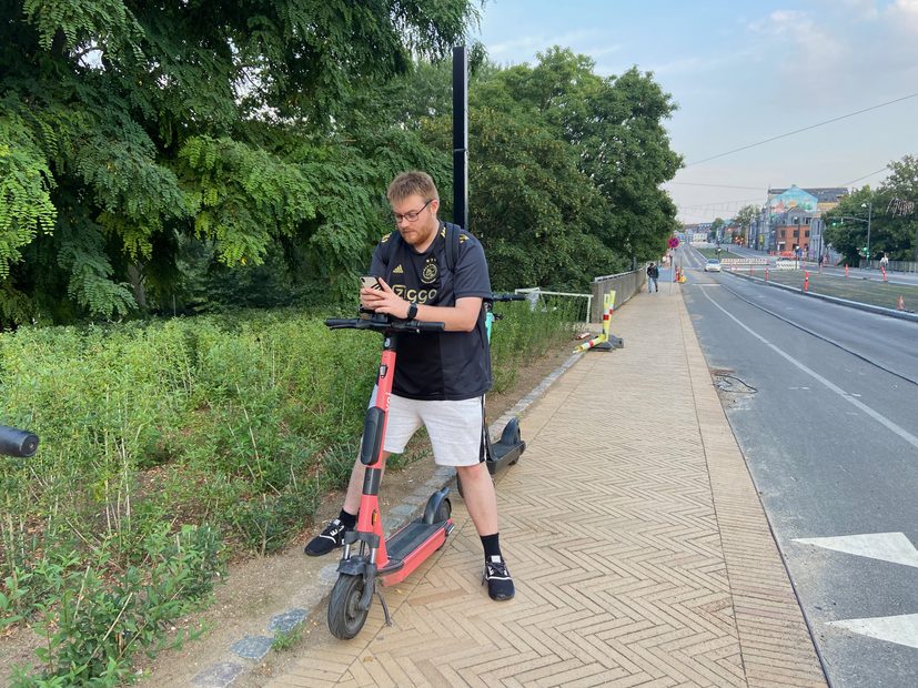 Voi Scooters Odense with Timo van den Berg standing next to a red shared electric scooter on a city sidewalk in Odense Denmark