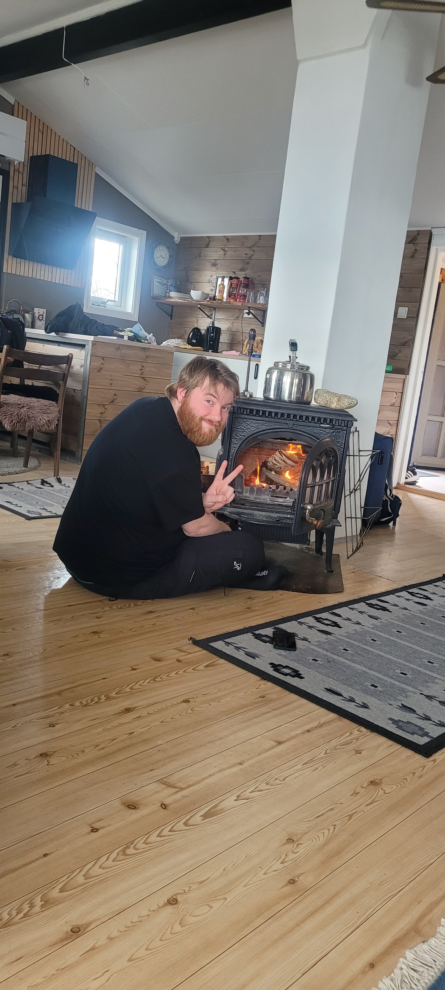 Northern Sweden Airbnb review, Timo van den Berg sitting beside the warm black fireplace inside a spacious wooden Airbnb cabin in Sweden