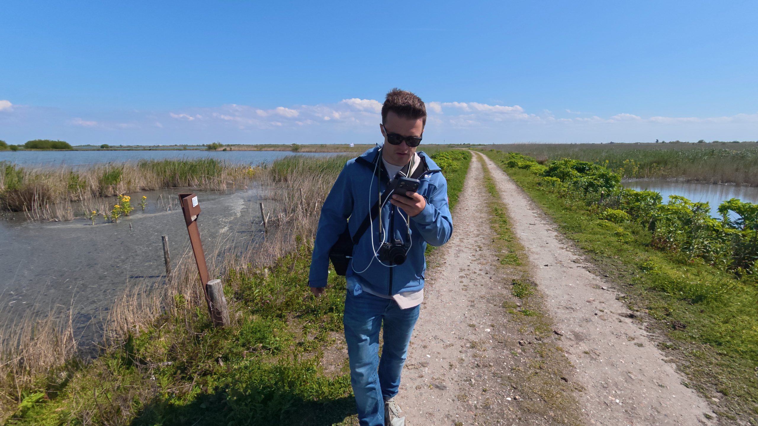 Pokémon GO Marker Wadden player Peter Smit checking a phone on a quiet nature trail between reeds and water during gameplay