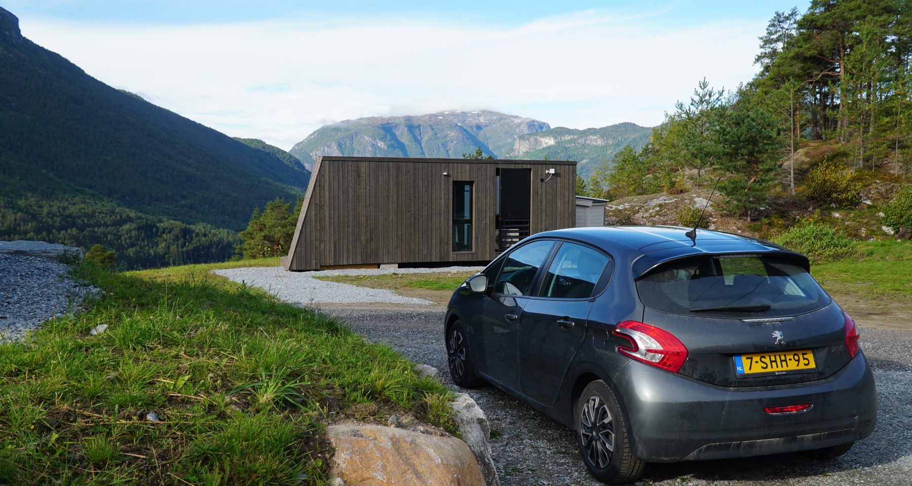 Peugeot 208 parked beside a modern cabin during a Sogndal Fjordpanorama Review in Norway, with mountain views and green fjord landscape