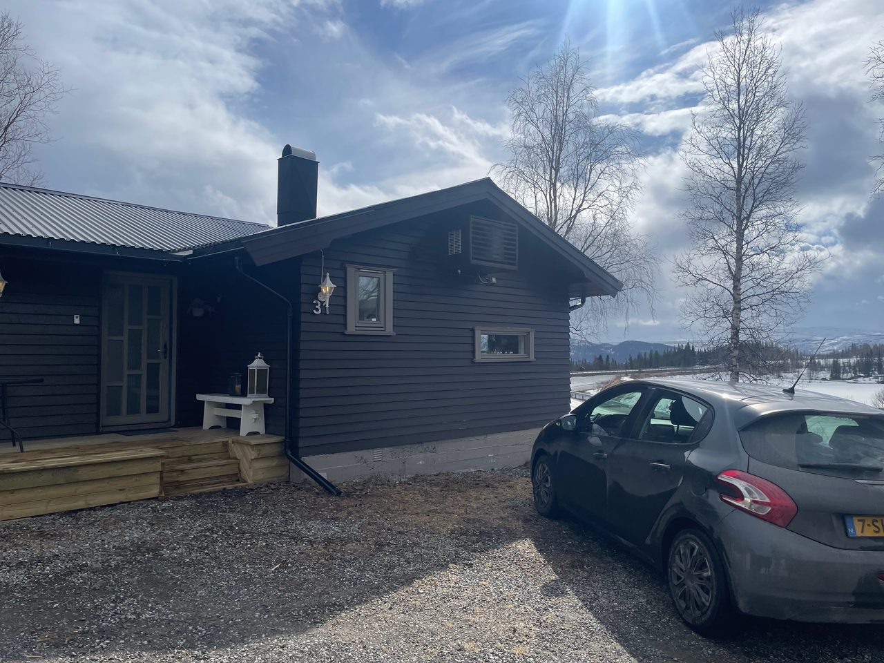 Northern Sweden Airbnb review, Peugeot 208 parked outside a dark wooden Airbnb cabin surrounded by snowy nature and bright Swedish sky