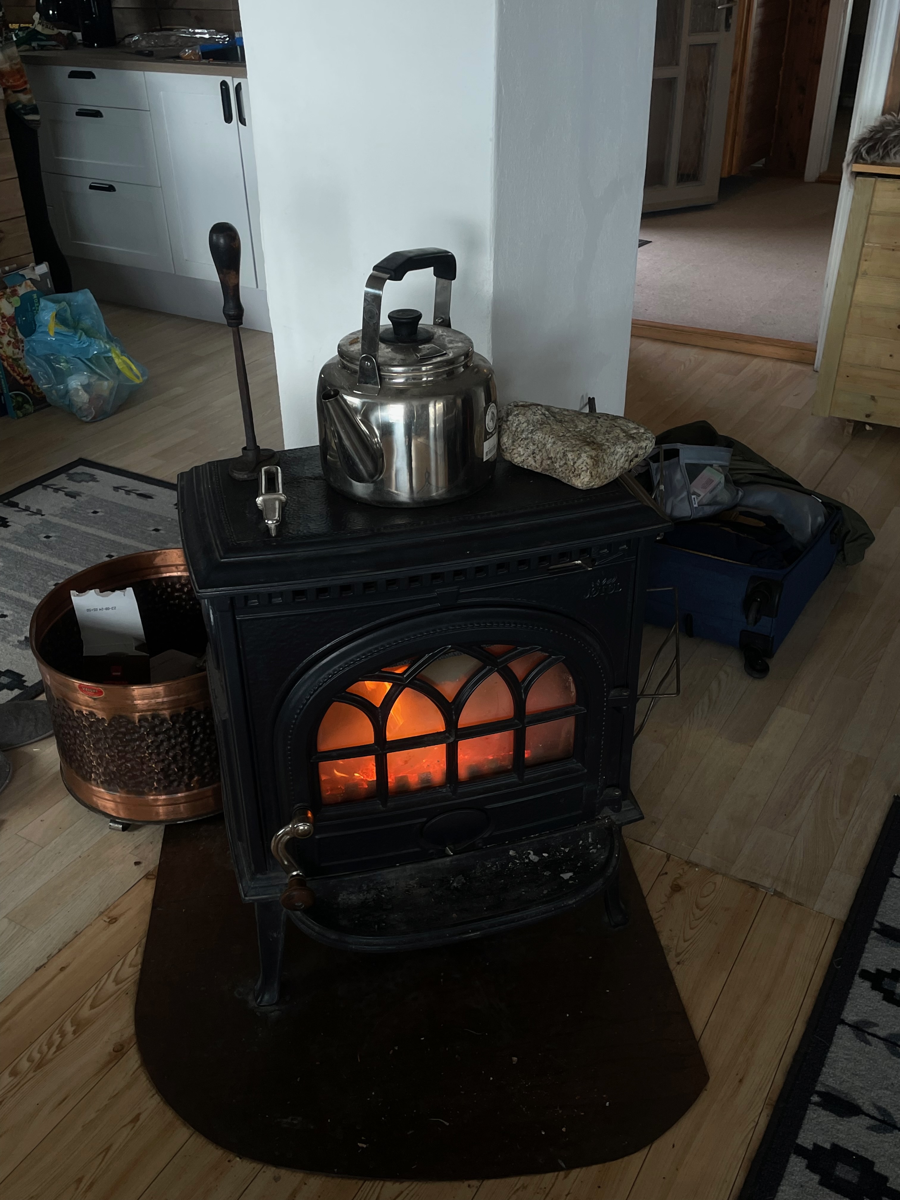 Northern Sweden Airbnb review, black wood-burning fireplace with glowing fire, kettle on top, and travel bags inside a rustic Swedish Airbnb