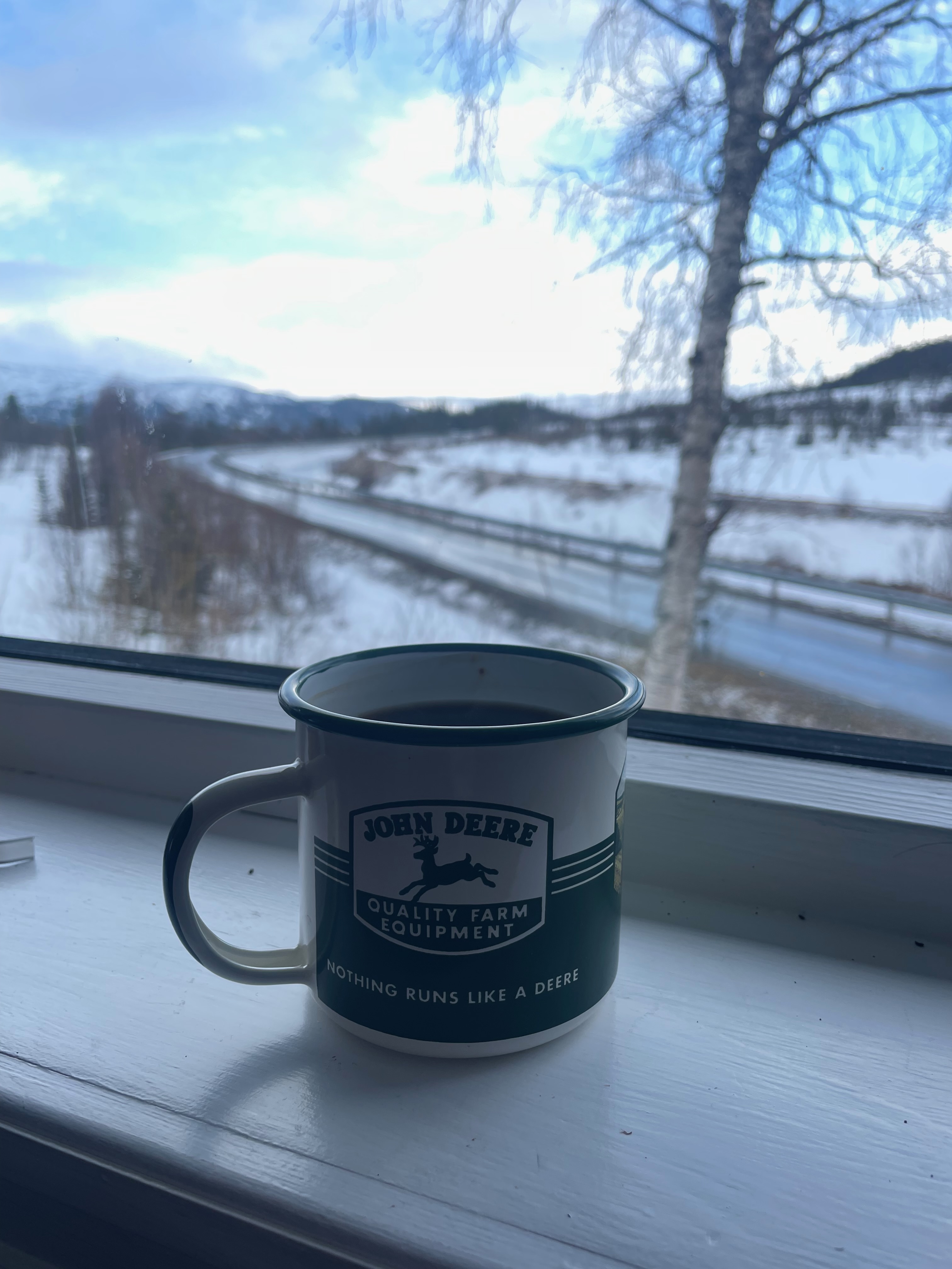 Northern Sweden Airbnb review, John Deere mug on the windowsill inside the Airbnb with a snowy Swedish road, trees, and winter landscape visible outside