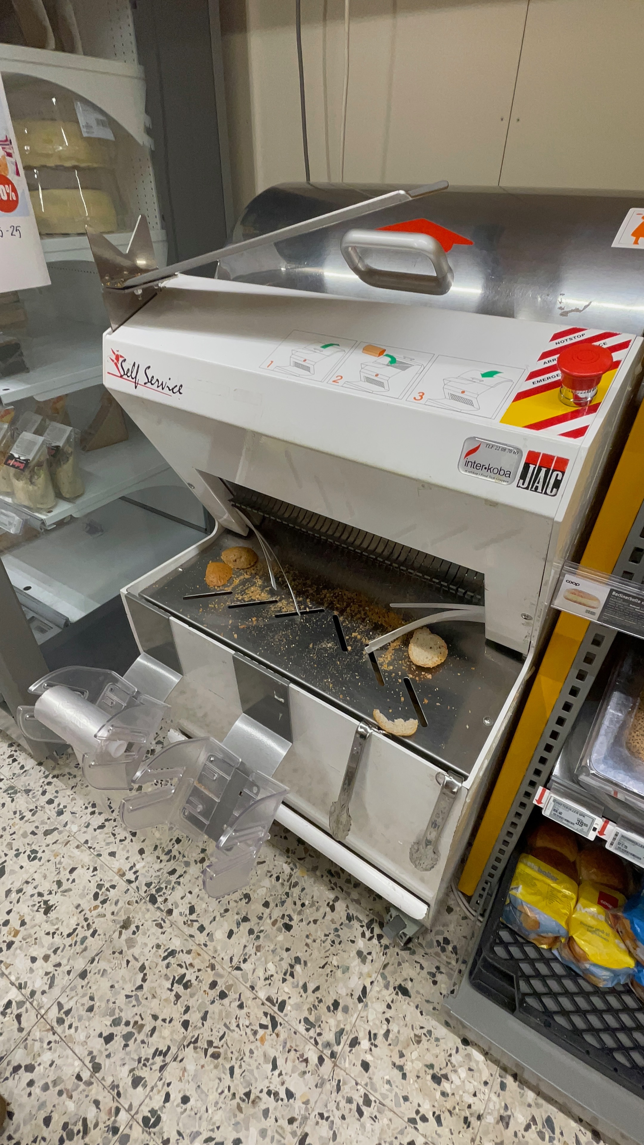 Bread slicing machine inside Extra Halsøy supermarket in Mosjøen, Norway, showing sliced bread crumbs, shelves, and the practical in-store bakery area for travelers.