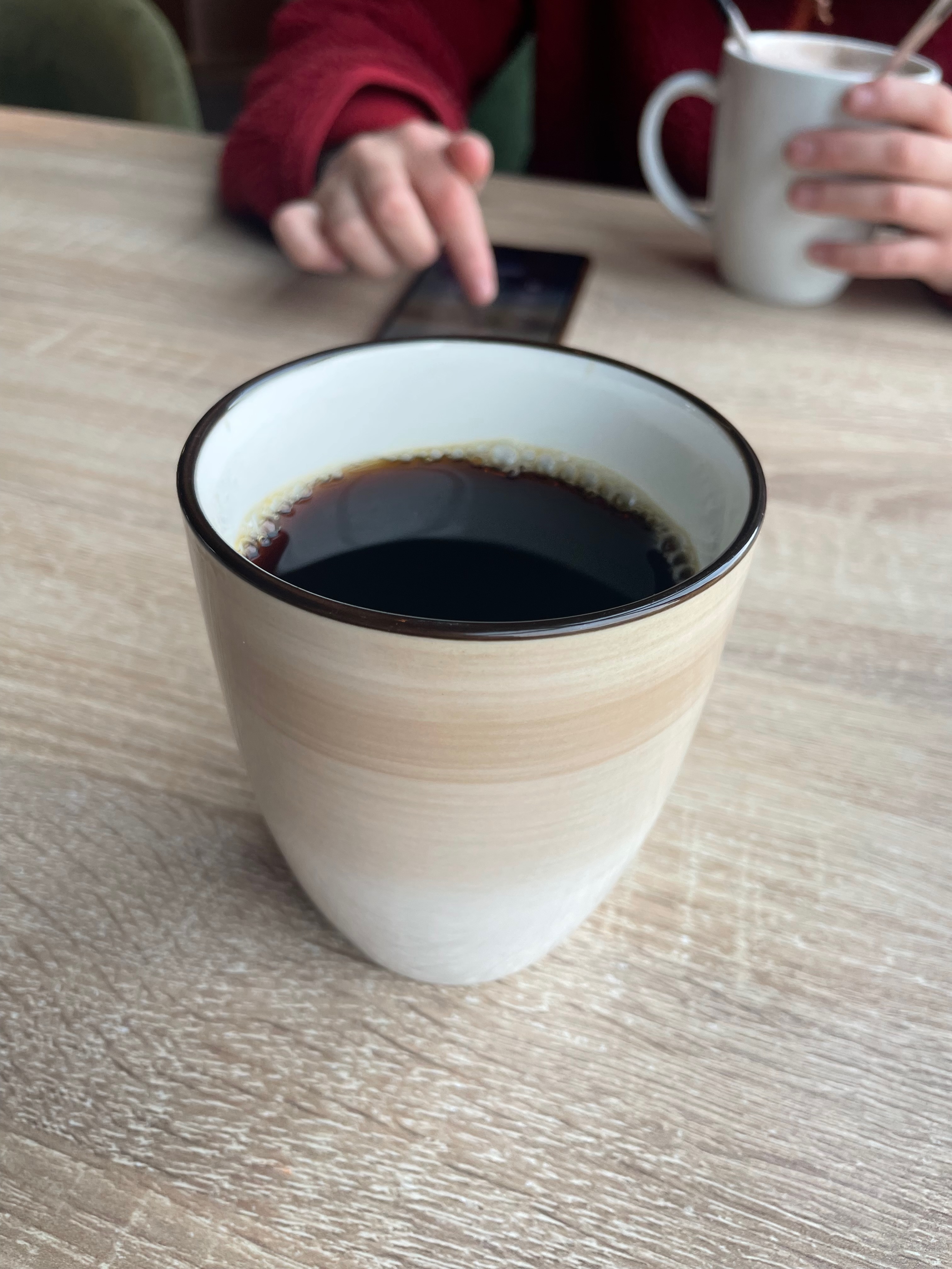 Cafe Sjøsiden in Mosjøen, close-up of black coffee on a café table with hot chocolate in the background during a Norway road trip stop.