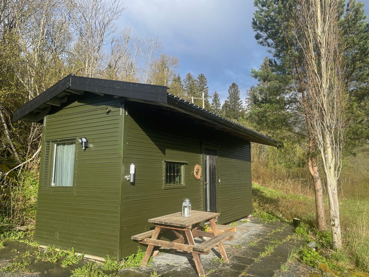 Airbnb in Stjordal Norway, green wooden countryside cabin in Stjørdal with a picnic table outside, surrounded by trees and nature during a quiet road trip stay.