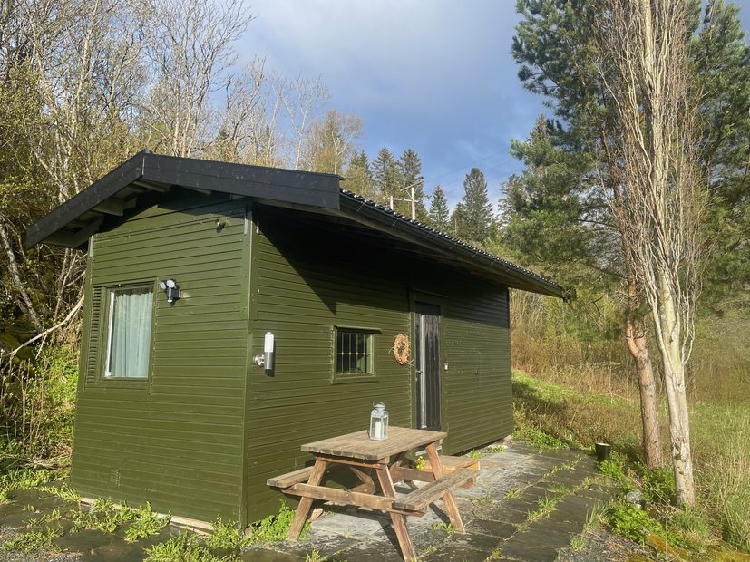 Airbnb in Stjordal Norway, green wooden countryside cabin in Stjørdal with a picnic table outside, surrounded by trees and nature during a quiet road trip stay.
