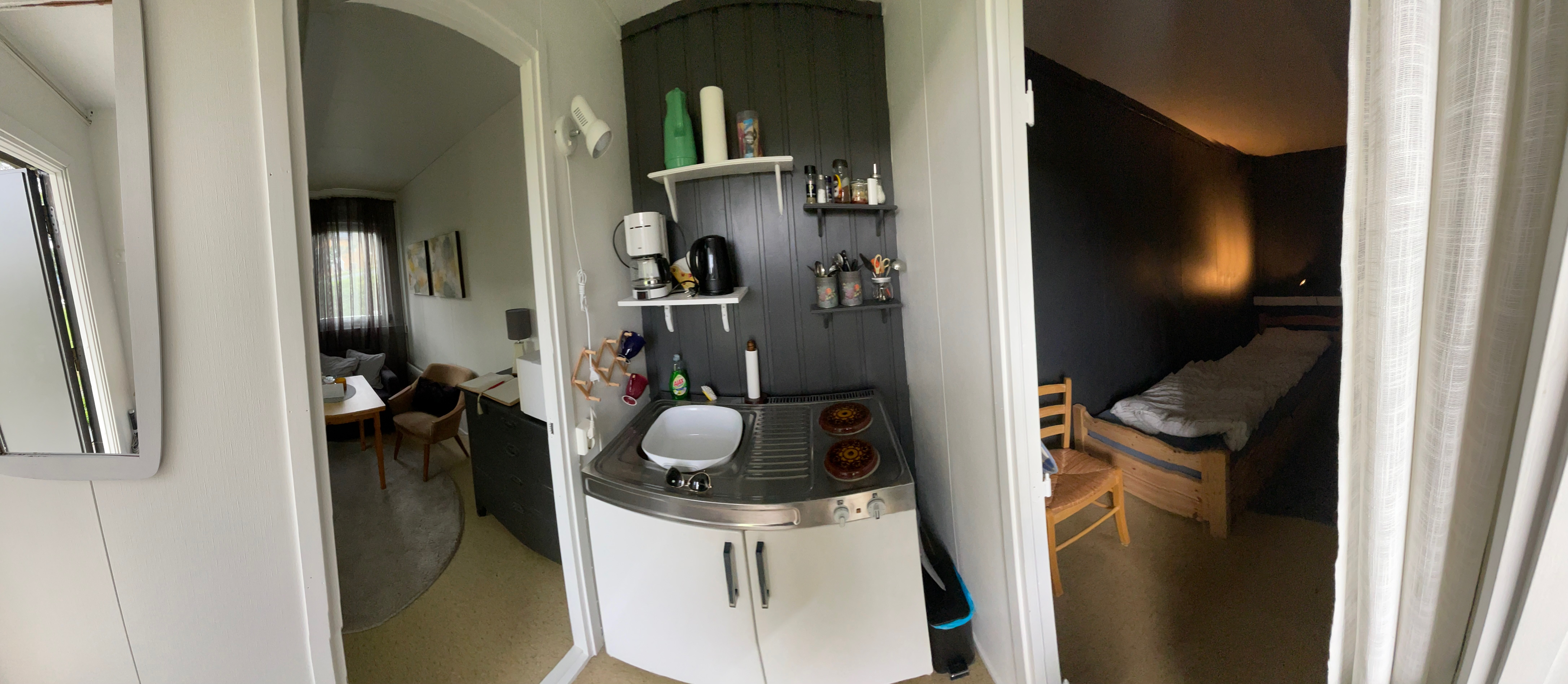 Airbnb in Stjordal Norway, simple cabin interior with a compact kitchenette, small living room, mirror, and dark separate bedroom with two wooden single beds.
