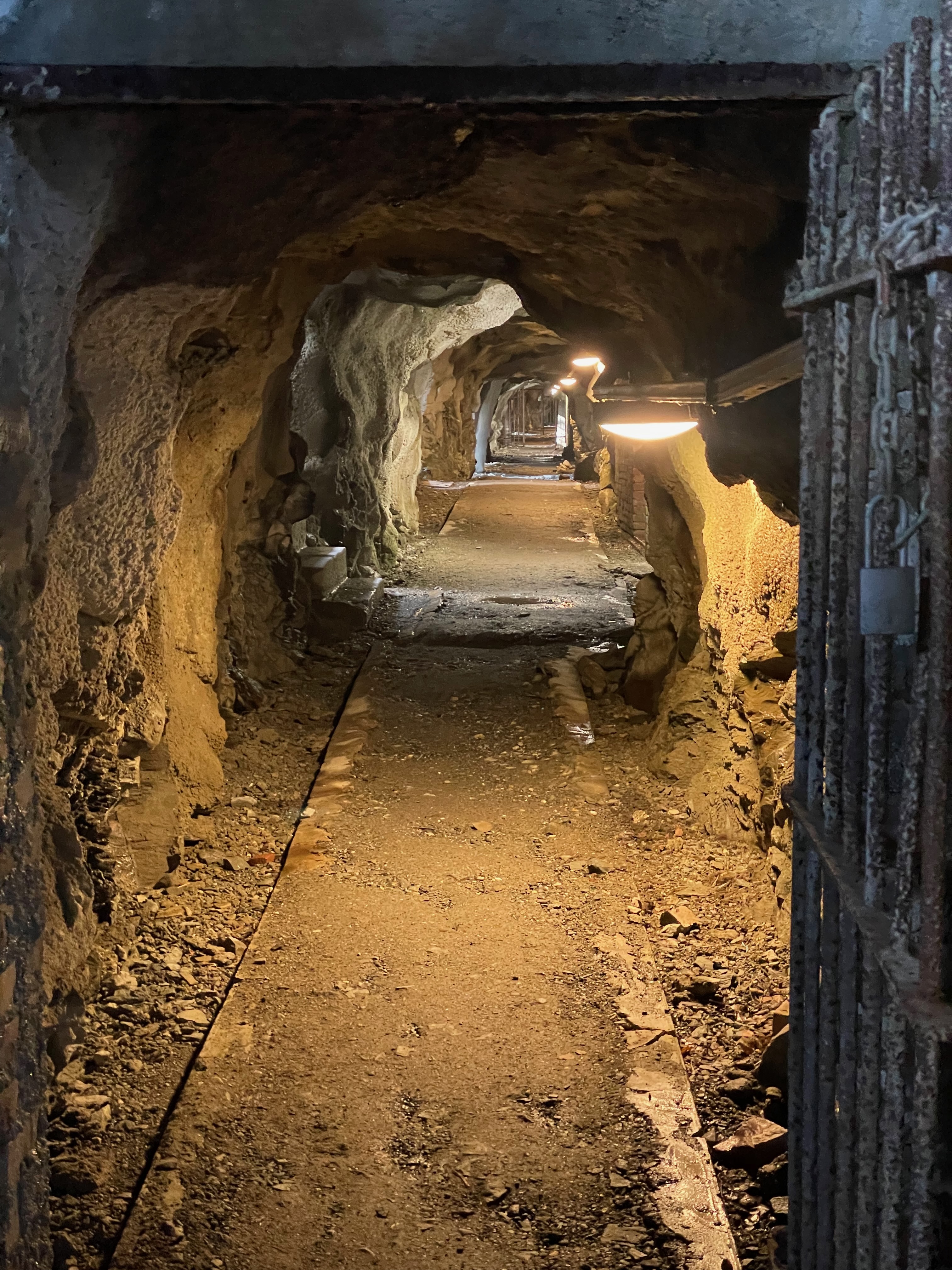 Hegra Fortress underground corridor in Norway, showing rocky tunnel walls, old concrete structures, metal doors, and historic military passageways