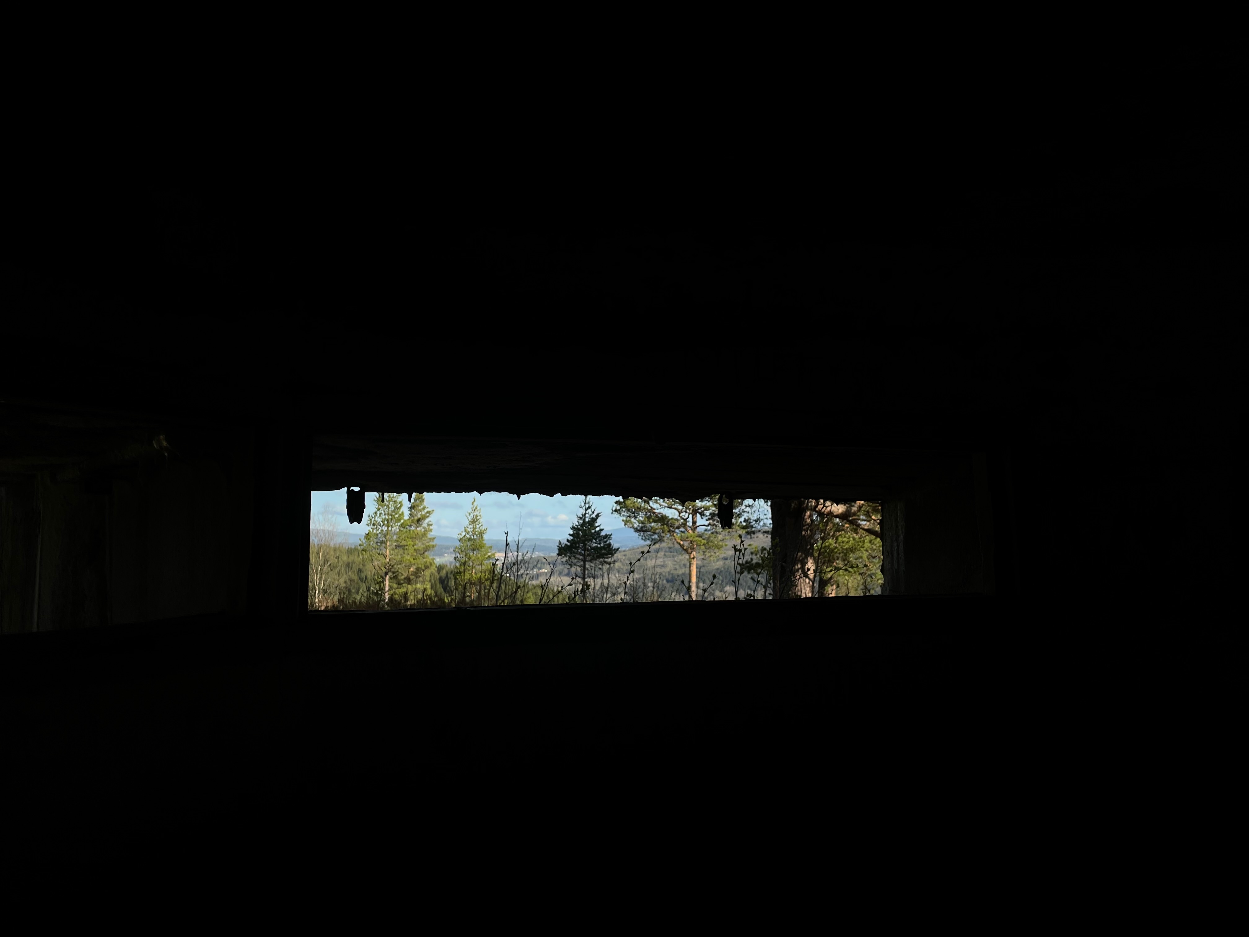 Hegra Fortress observation slit inside the historic fort, with a dark bunker interior and a narrow view toward the forested Norwegian landscape
