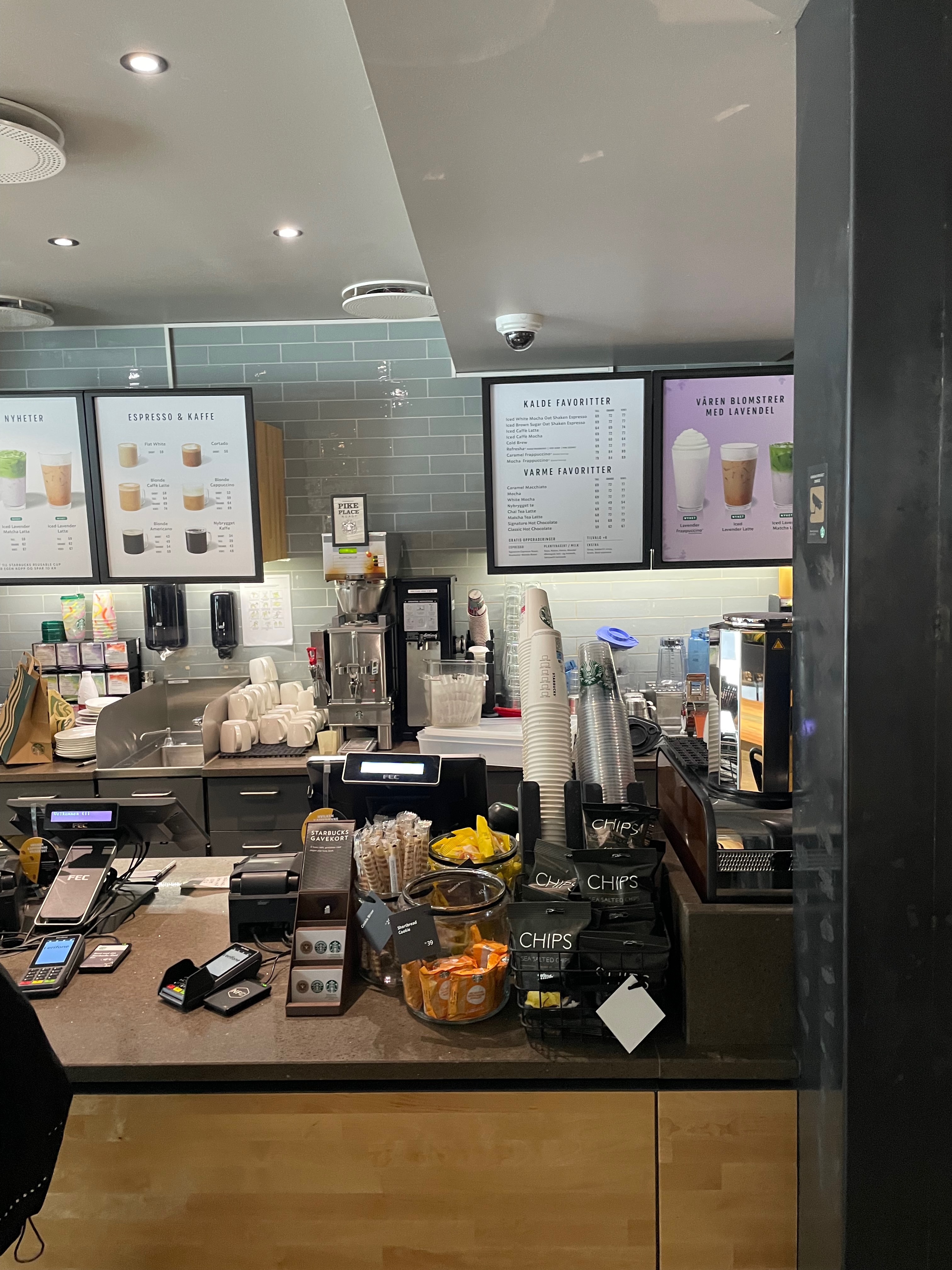Starbucks Trondheim counter with menu screens, coffee machines, takeaway cups, snacks, chips, and ordering area inside the café.