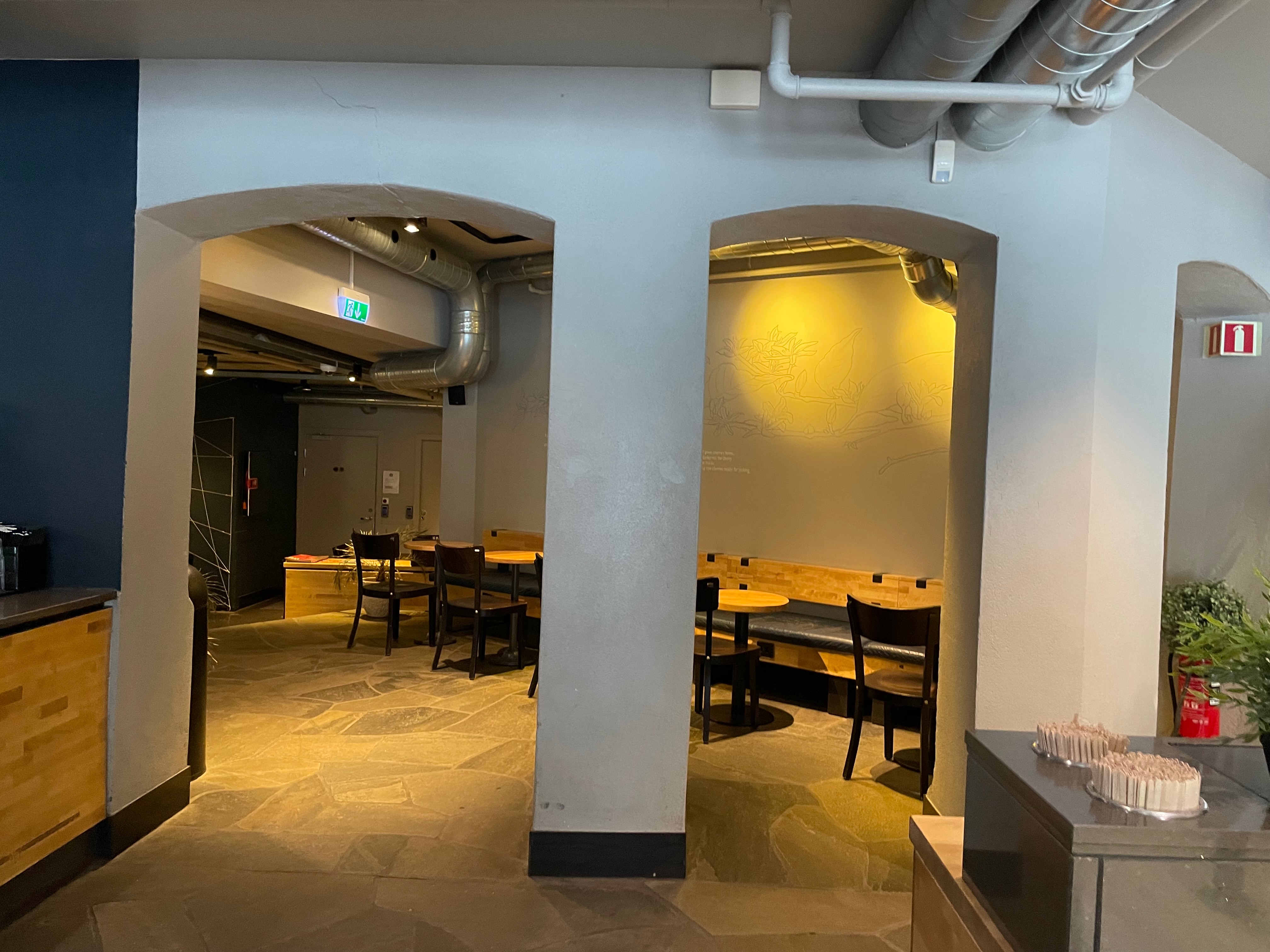 Starbucks Trondheim seating area with arched walls, warm lighting, wooden tables, benches, and a quiet restaurant space.