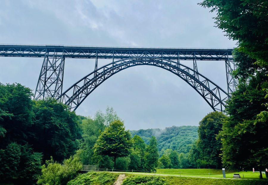 Müngstener Brücke towering above the green Brückenpark Müngsten valley in Solingen, Germany, with forest views and cloudy skies.