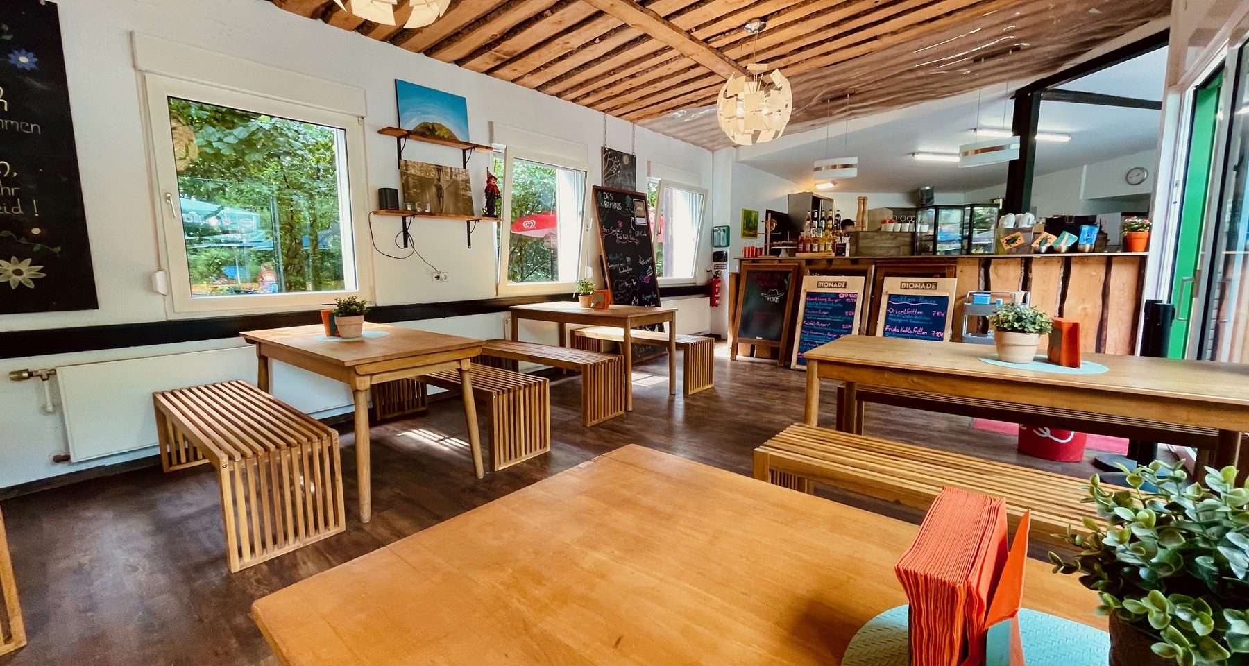 Das Baumhaus Kletterbistro interior with wooden tables, benches, plants, menu boards, and a relaxed forest bistro atmosphere at Wald Abenteuer Velbert Langenberg