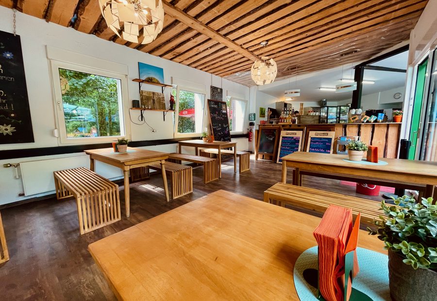 Das Baumhaus Kletterbistro interior with wooden tables, benches, plants, menu boards, and a relaxed forest bistro atmosphere at Wald Abenteuer Velbert Langenberg