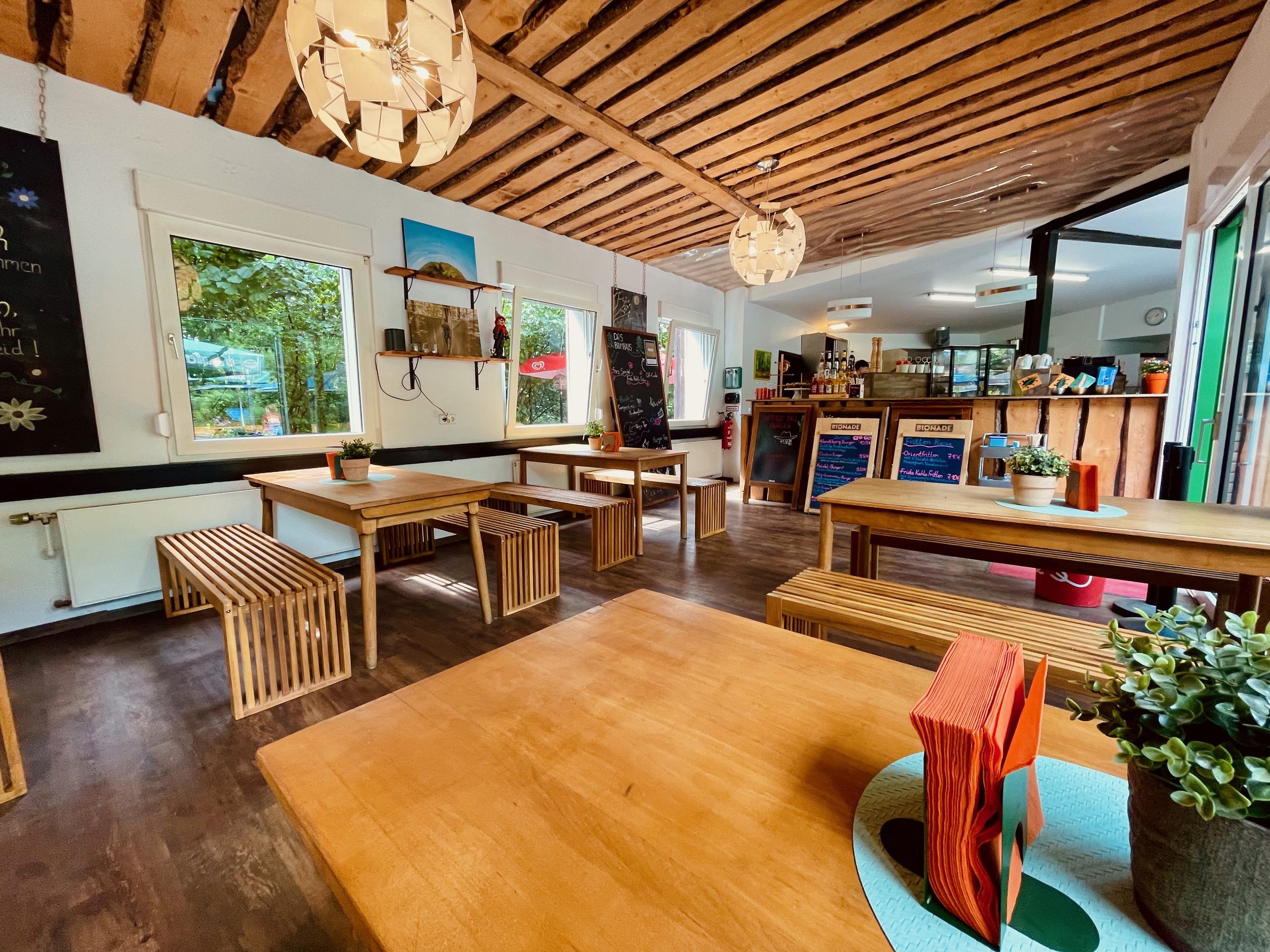 Das Baumhaus Kletterbistro interior with wooden tables, benches, plants, menu boards, and a relaxed forest bistro atmosphere at Wald Abenteuer Velbert Langenberg