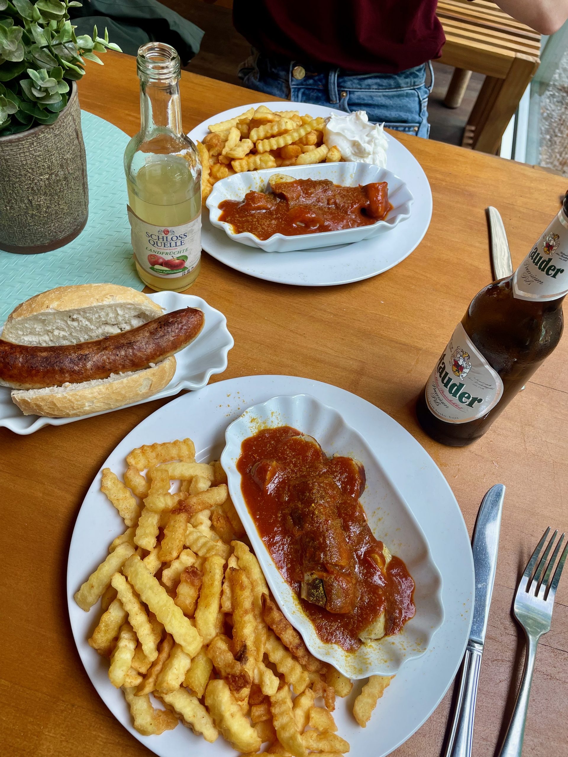 Das Baumhaus Kletterbistro currywurst with fries, bratwurst in a bread roll, Schlos Quelle apple spritzer, and Almdudler served on a wooden table