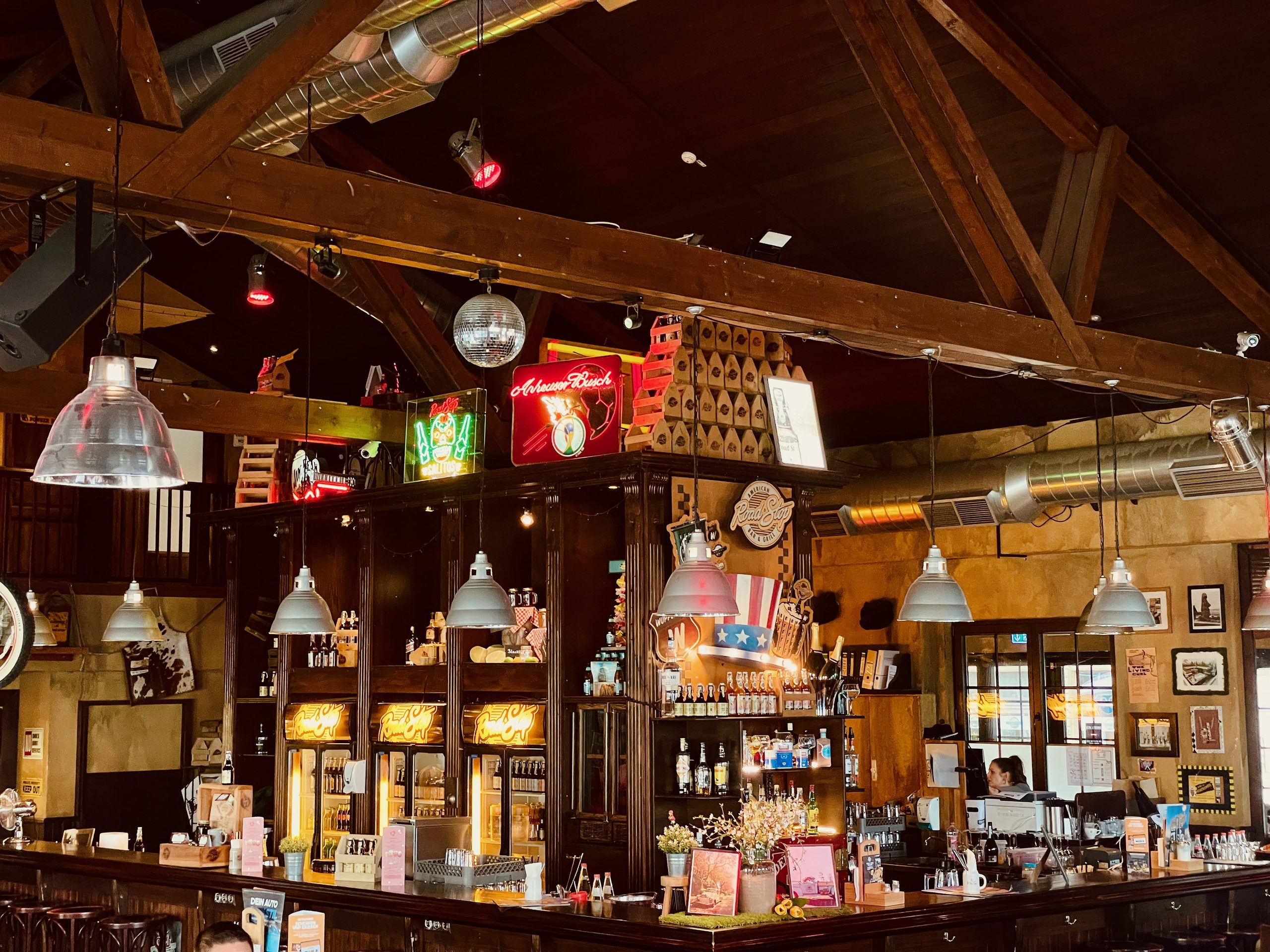 Road Stop Wuppertal bar area with wooden beams, neon signs, beer taps, hanging lamps, and an American road house atmosphere inside the restaurant.