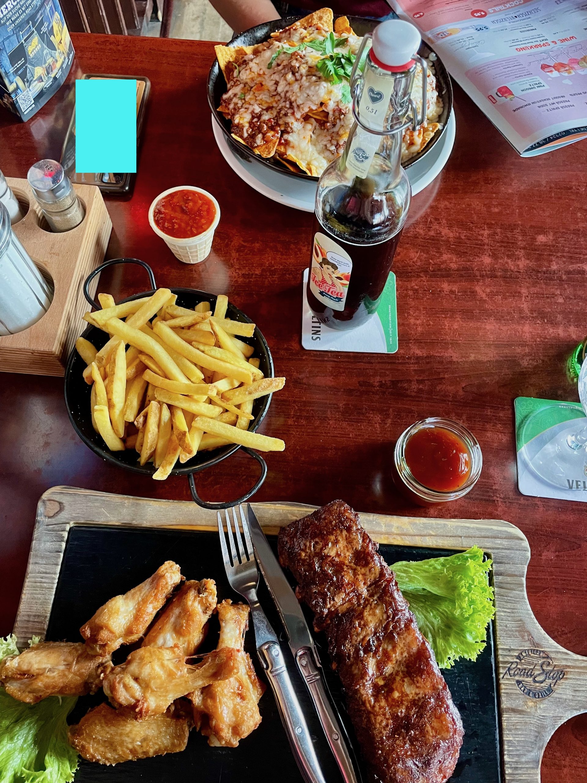 Road Stop Wuppertal dinner table with Texas Ribs, chicken wings, fries, nachos, sauces, and drinks inside the American style restaurant.