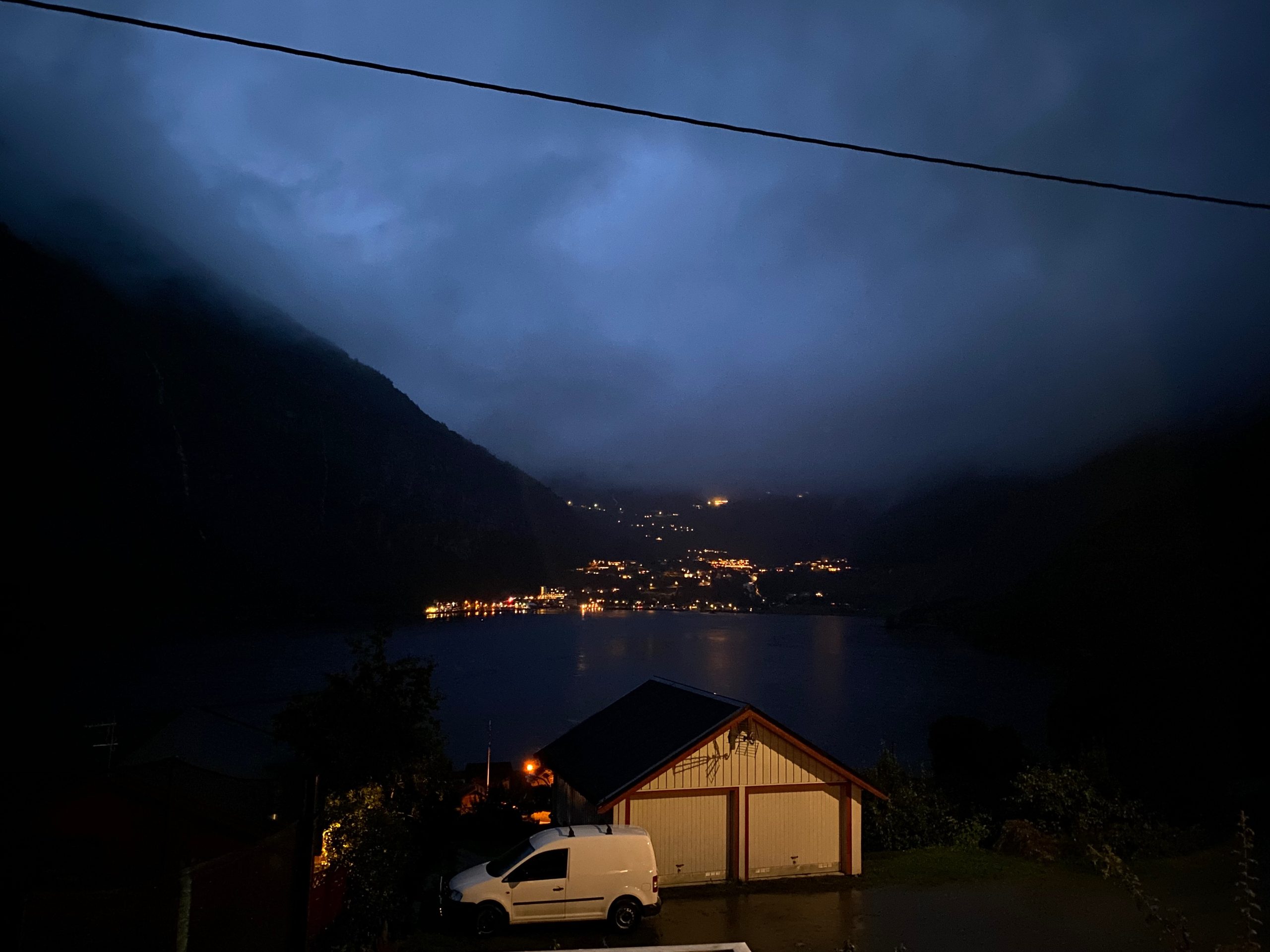Geiranger Airbnb evening view over Geirangerfjord with village lights, dark mountains, low clouds, and rainy Norwegian fjord scenery