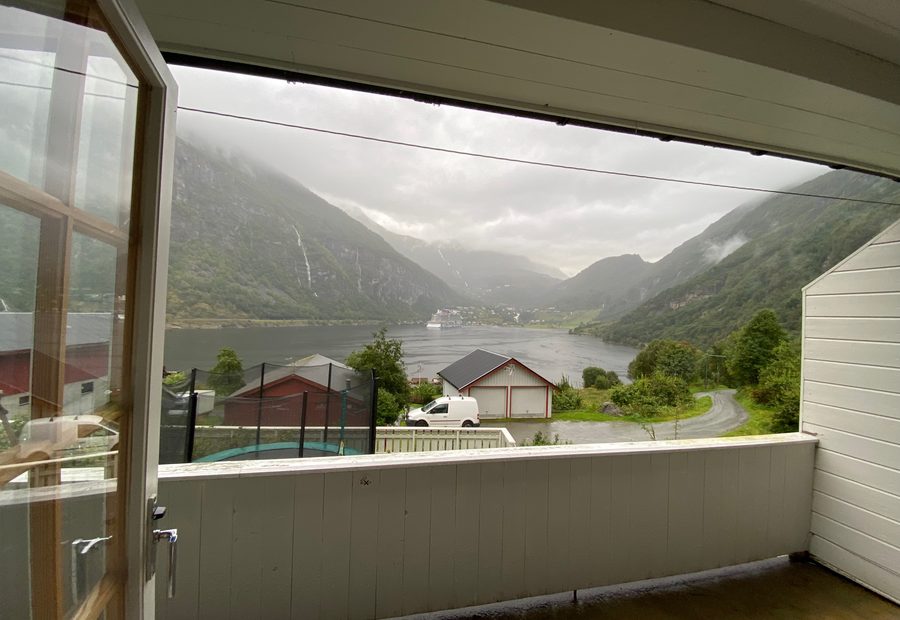 Geiranger Airbnb balcony view overlooking Geirangerfjord, mountain waterfalls, cloudy fjord weather, and the village of Geiranger in Norway