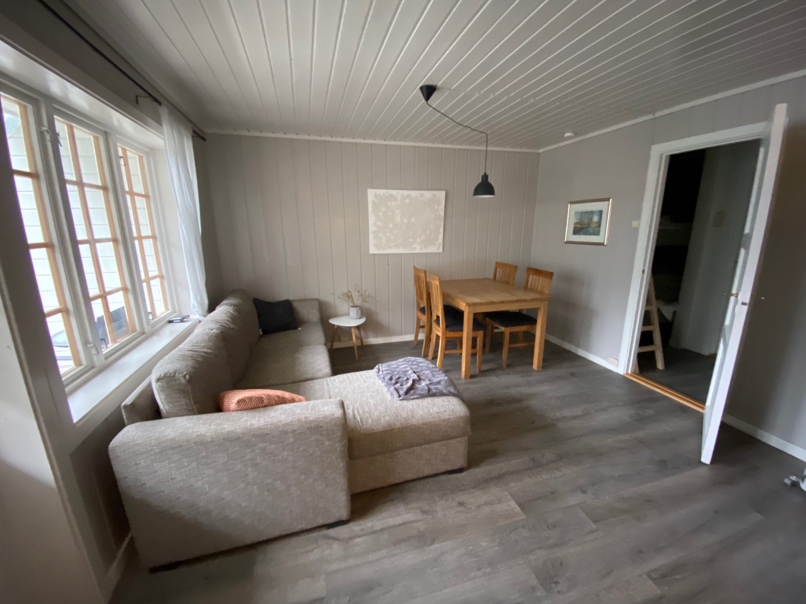 Geiranger Airbnb living room with sofa, dining table, wooden chairs, large windows, and simple Scandinavian interior in the fjord view apartment