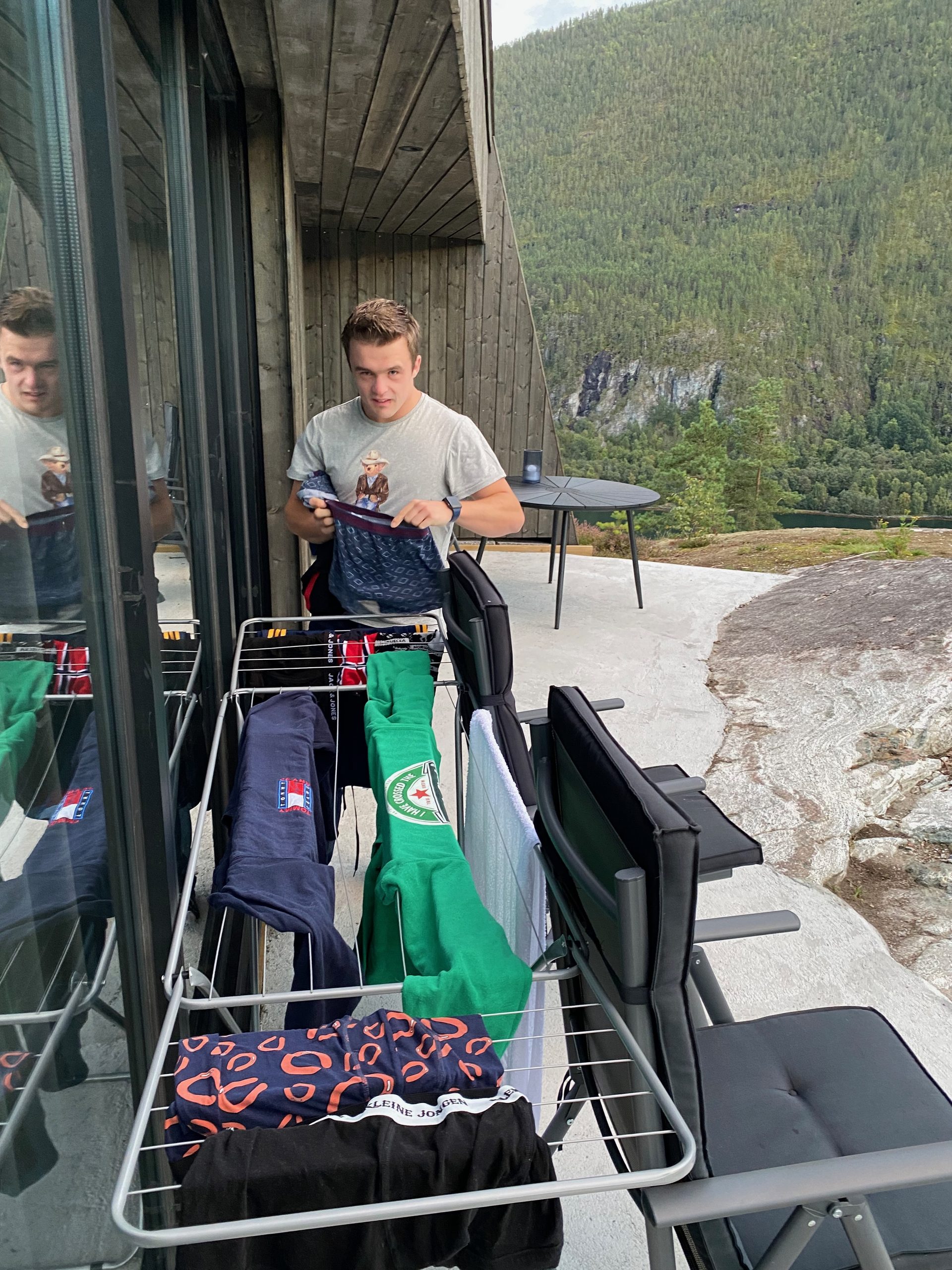 Peter Smit hanging laundry outside the cabin during a Sogndal Fjordpanorama Review in Norway, with terrace seating and mountain views