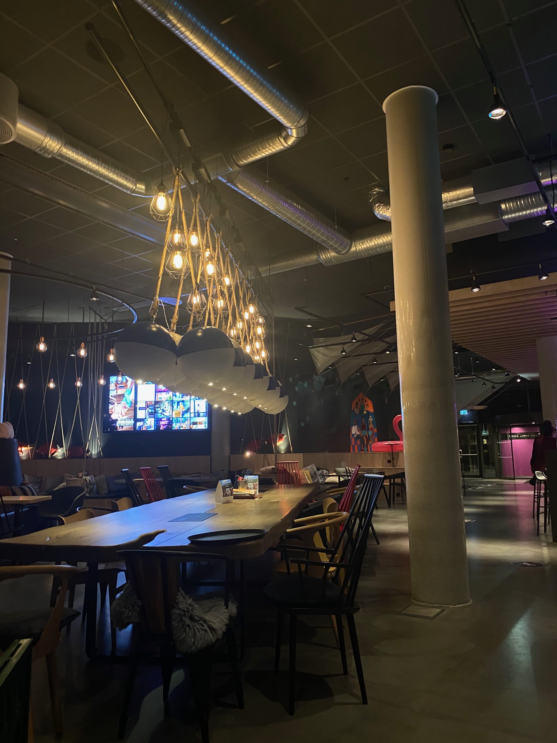 Moxy Hotel Bergen lobby with industrial lighting, colorful seating, long tables, and a modern social lounge atmosphere