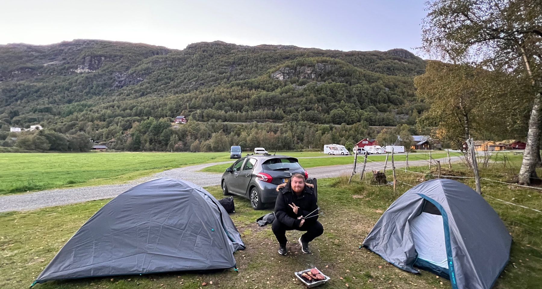 Timo van den Berg enjoying a simple barbecue evening between two tents at Seim Camping Røldal, surrounded by green fields and Norwegian mountains.