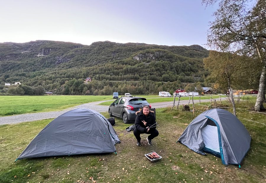 Timo van den Berg enjoying a simple barbecue evening between two tents at Seim Camping Røldal, surrounded by green fields and Norwegian mountains.