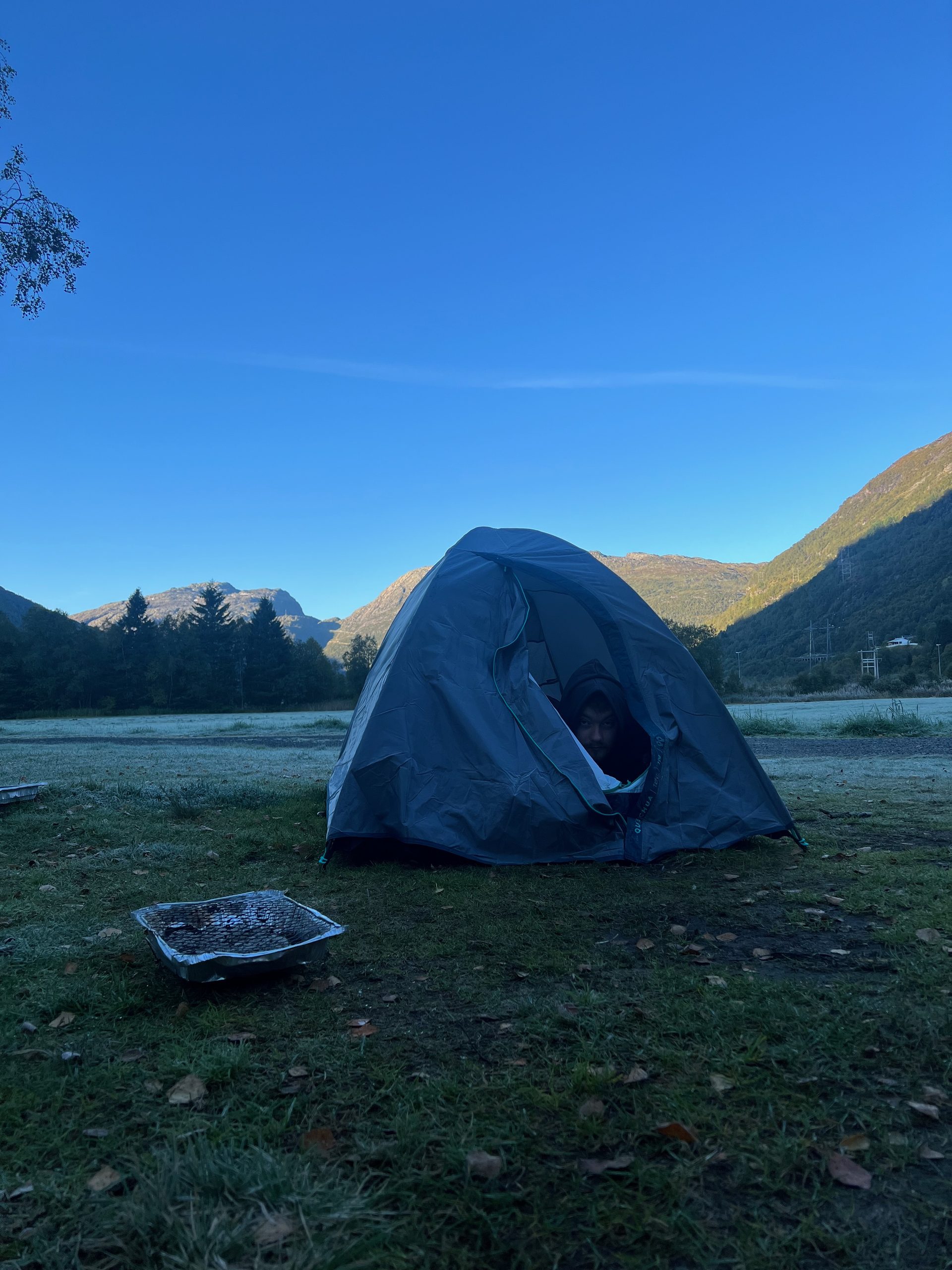 Morning tent view from Timo van den Berg at Seim Camping Røldal with frost on the grass, a disposable barbecue, and Norwegian mountain scenery.