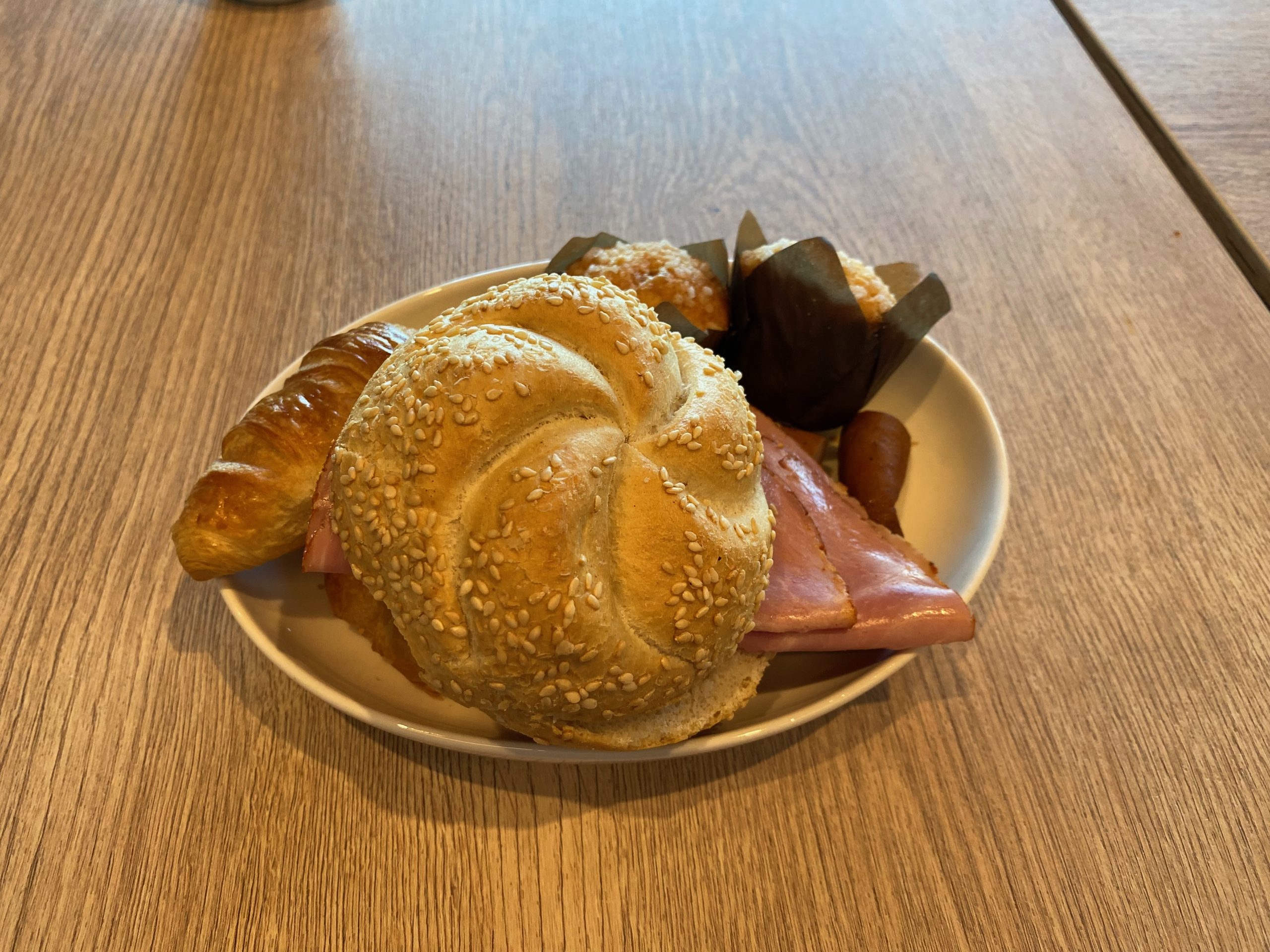 Moxy Hotel Bergen breakfast plate with a sesame bread roll, croissant, ham, muffin, and small sausage in Bergen