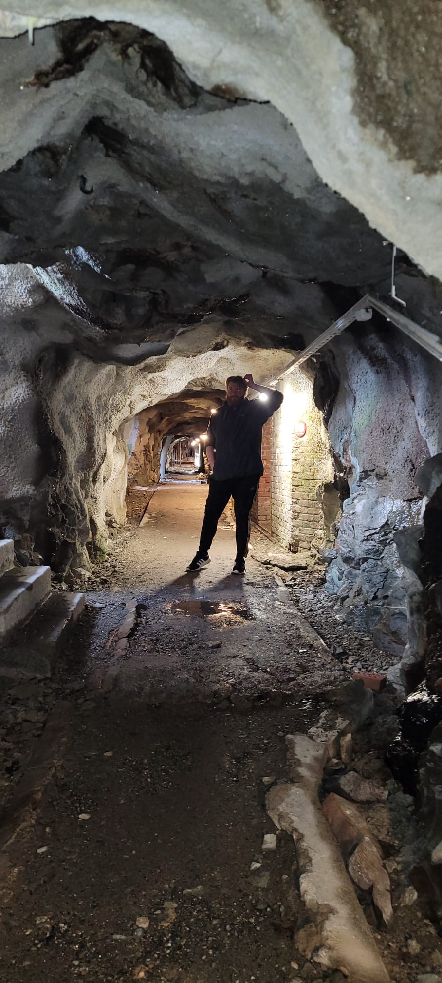 Traveler standing inside the rocky underground tunnel of Hegra Fortress in Norway, with rough cave walls, old concrete passages, and warm bunker lights