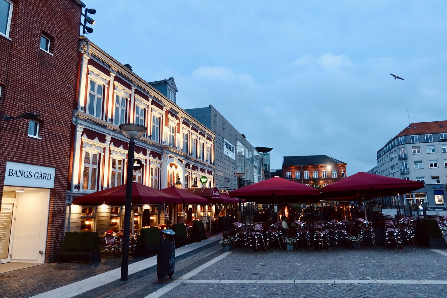 Dronning Louise Esbjerg Review terrace on Torvet in Esbjerg Denmark with red umbrellas historic buildings and evening city atmosphere