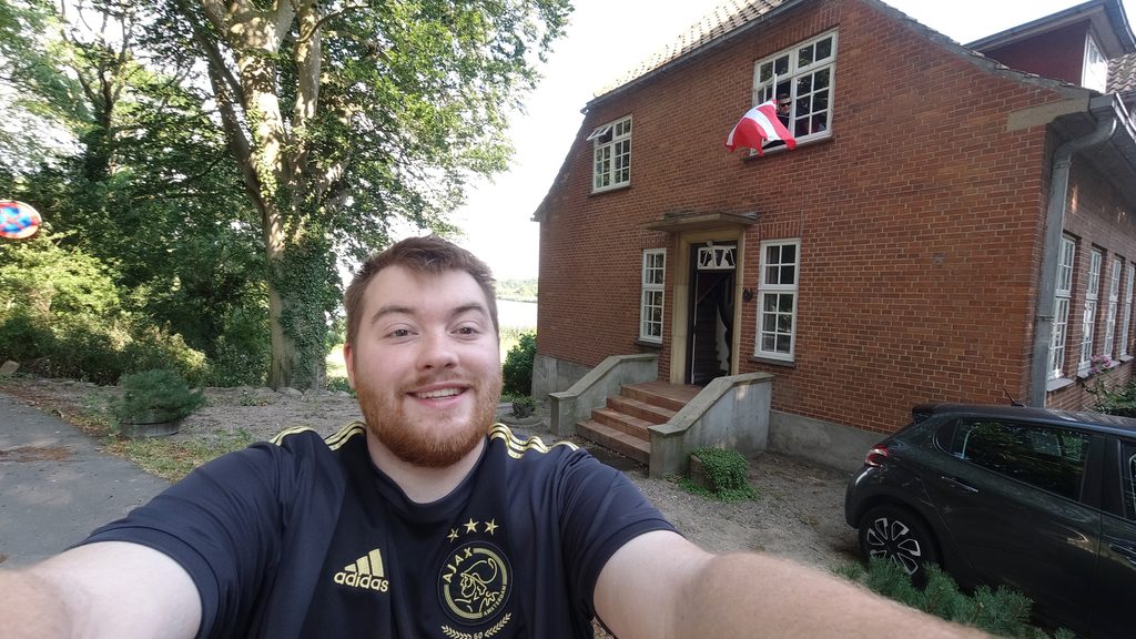 Mjelsgaard 1 Airbnb Review showing Timo van den Berg taking an arrival selfie in front of the red brick Airbnb house in Denmark, with a Peugeot 208 parked outside and the upstairs room visible