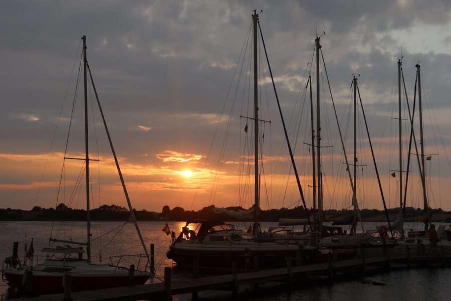 Mjelsvig Harbor at sunset with sailboats, dark clouds, calm water, and a warm orange sky in Mjels Denmark